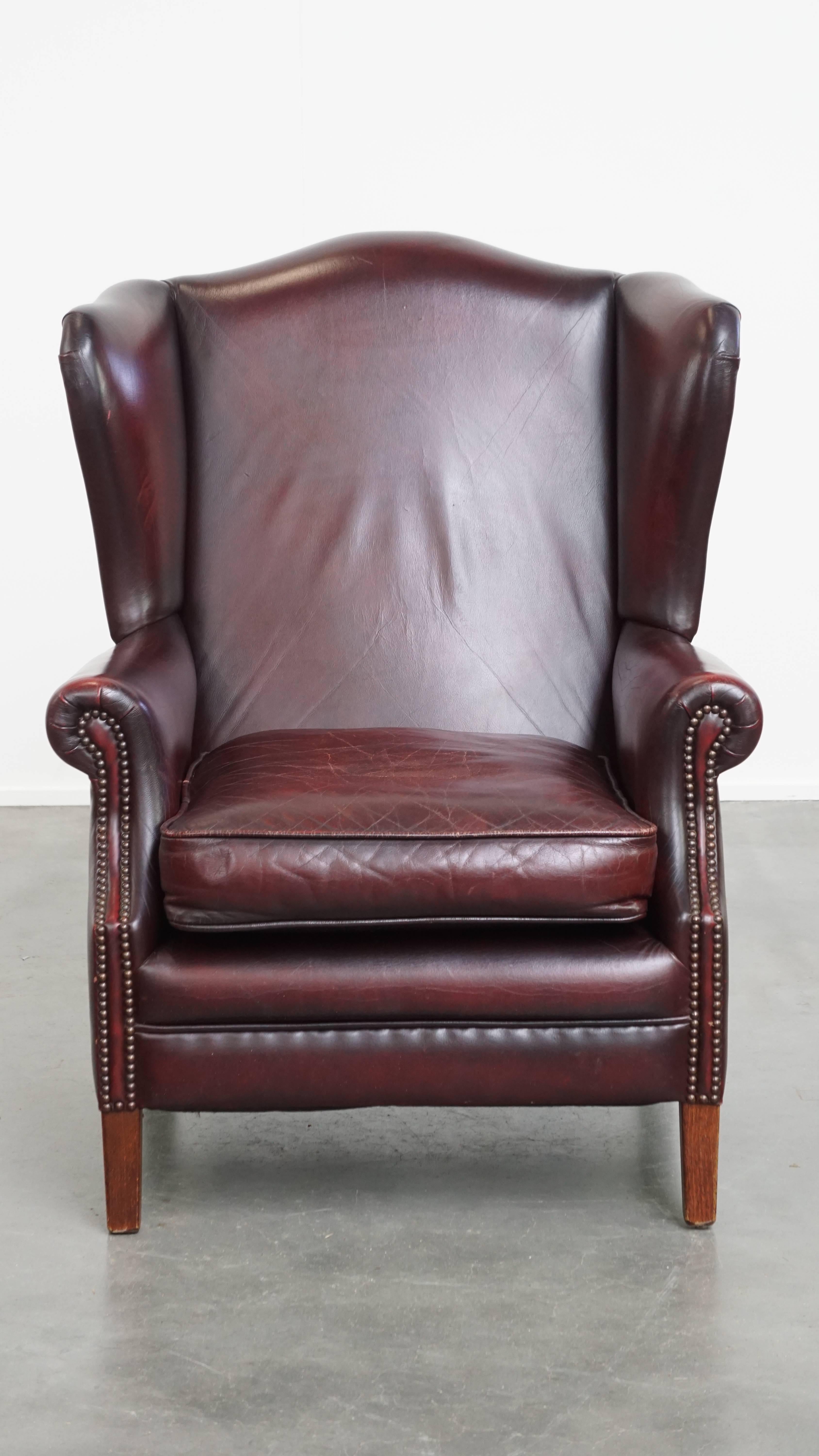 This charming and comfortable bordeaux red cowhide wingback armchair in English style, featuring a beautiful patina. This luxurious and comfortable armchair is crafted from high-quality cowhide leather and finished with decorative nailhead