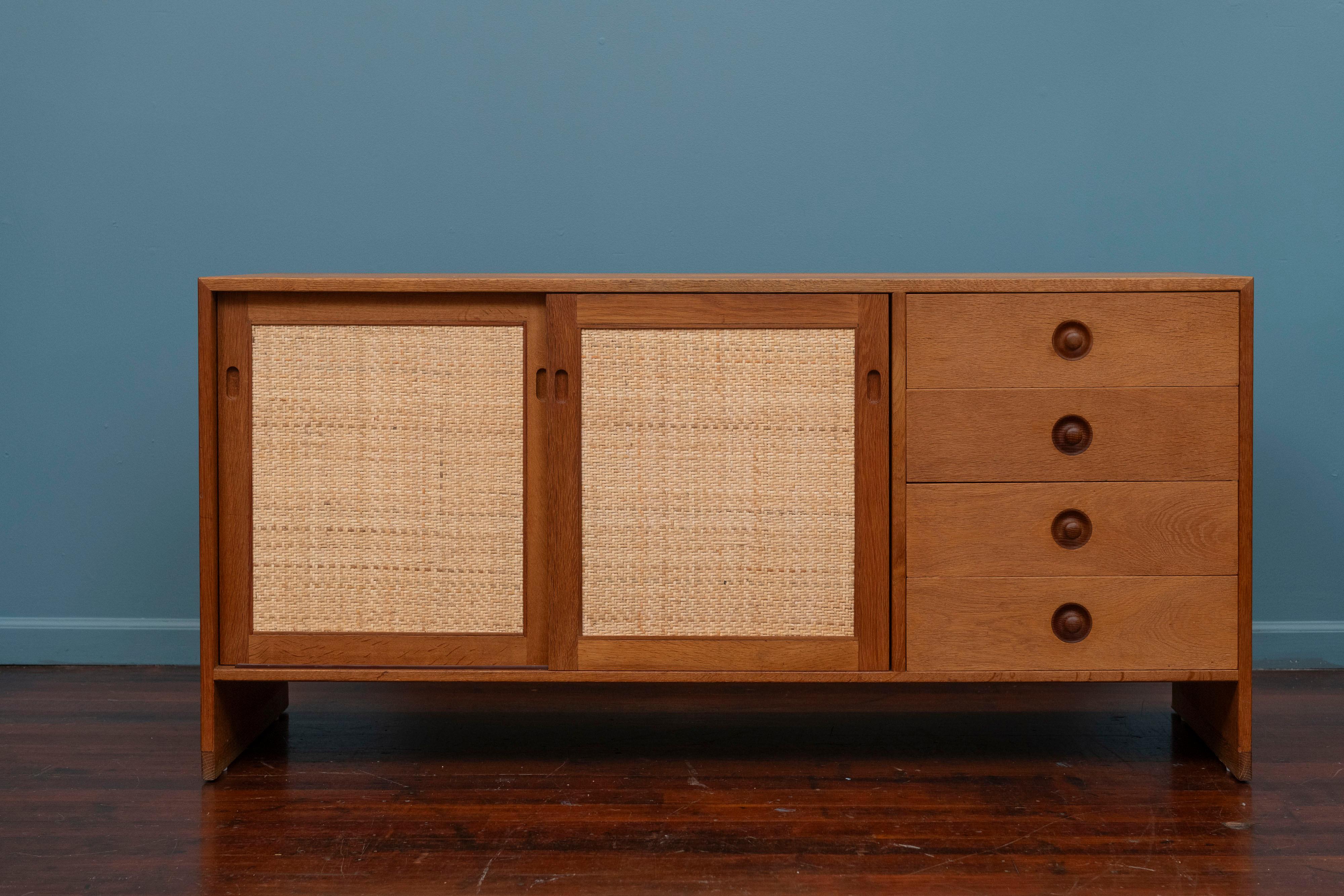 Borge Mogensen design credenza for Karl Anderson, Denmark. High quality construction materials featuring a white oak case with two caned sliding doors revealing ample storage and two adjustable shelves. Four drawers with sculpted teak pulls that