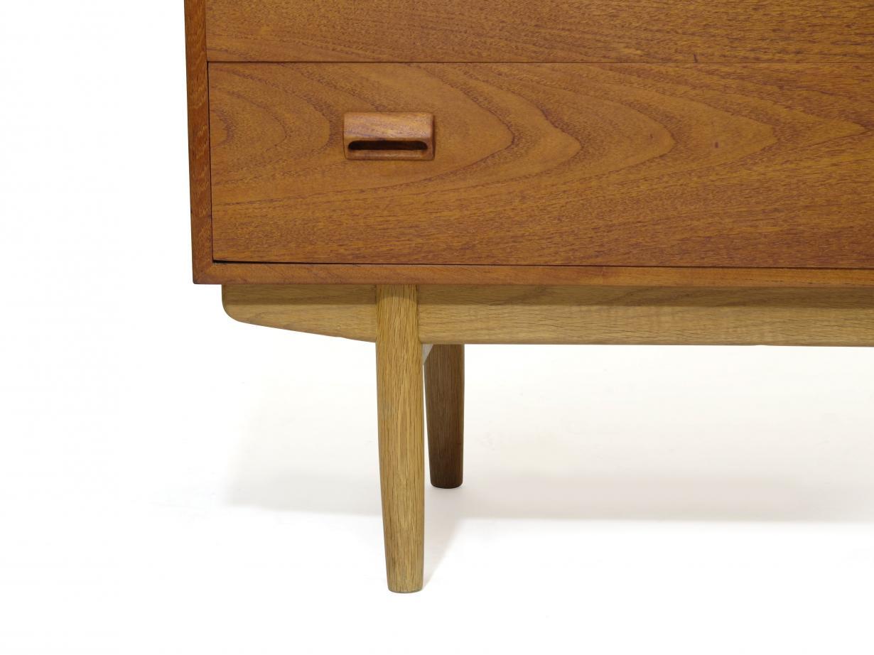 Midcentury teak vanity dresser designed by Borge Mogensen crafted of teak with three drawers, raised on white oak legs. The face of the top drawer flips down with the press of brass latch, and pulls-out for a spacious writing surface revealing a