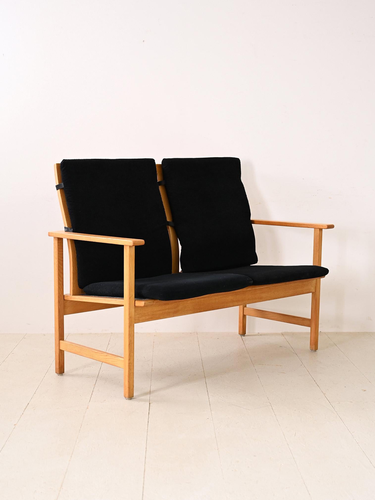 Two-seater sofa with oak wood frame. An original piece of Scandinavian modernism consisting of a simple wooden frame equipped with armrests and complemented by the original cushions found on the seat and back. The square, minimal lines make this