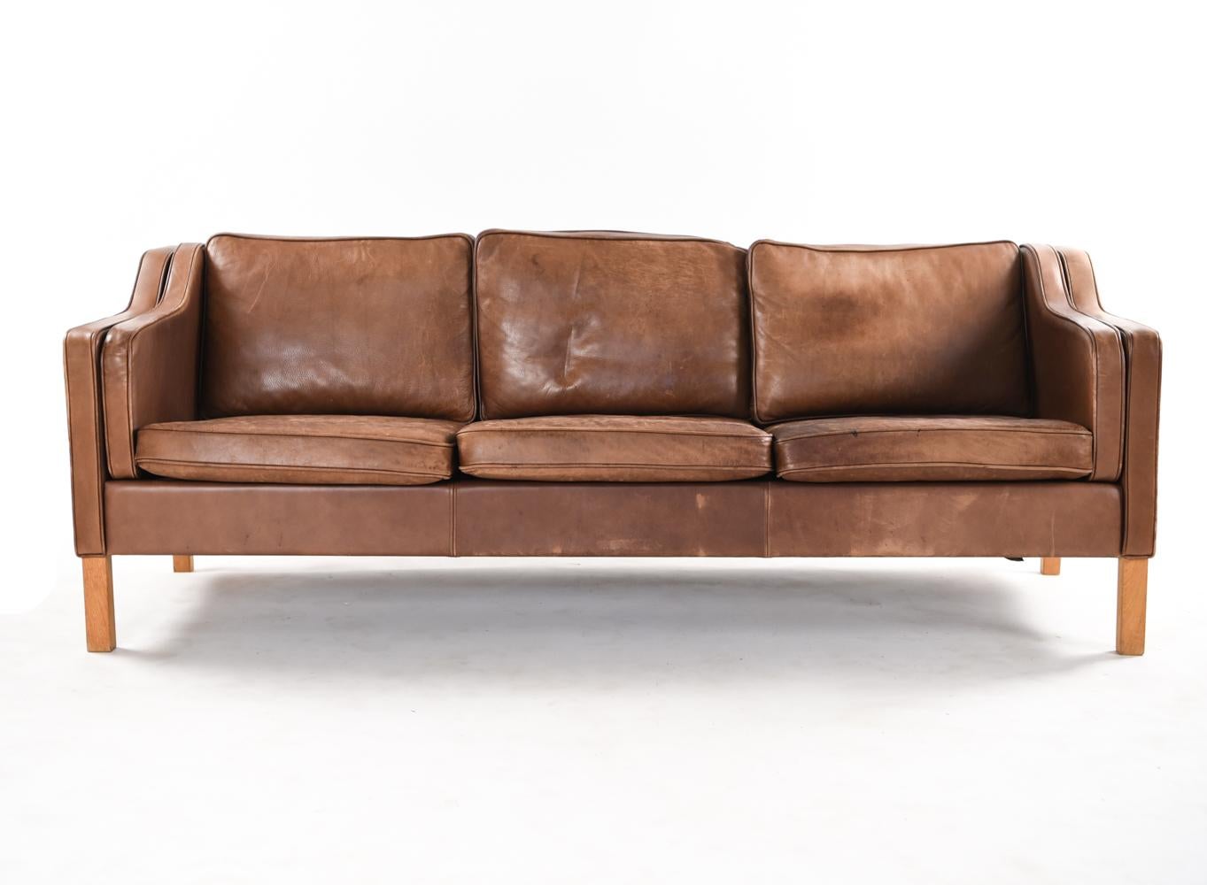 This attractive Danish midcentury three-seat sofa is in the manner of Borge Mogensen's timeless design. The brown leather displays a lovely patination from age.