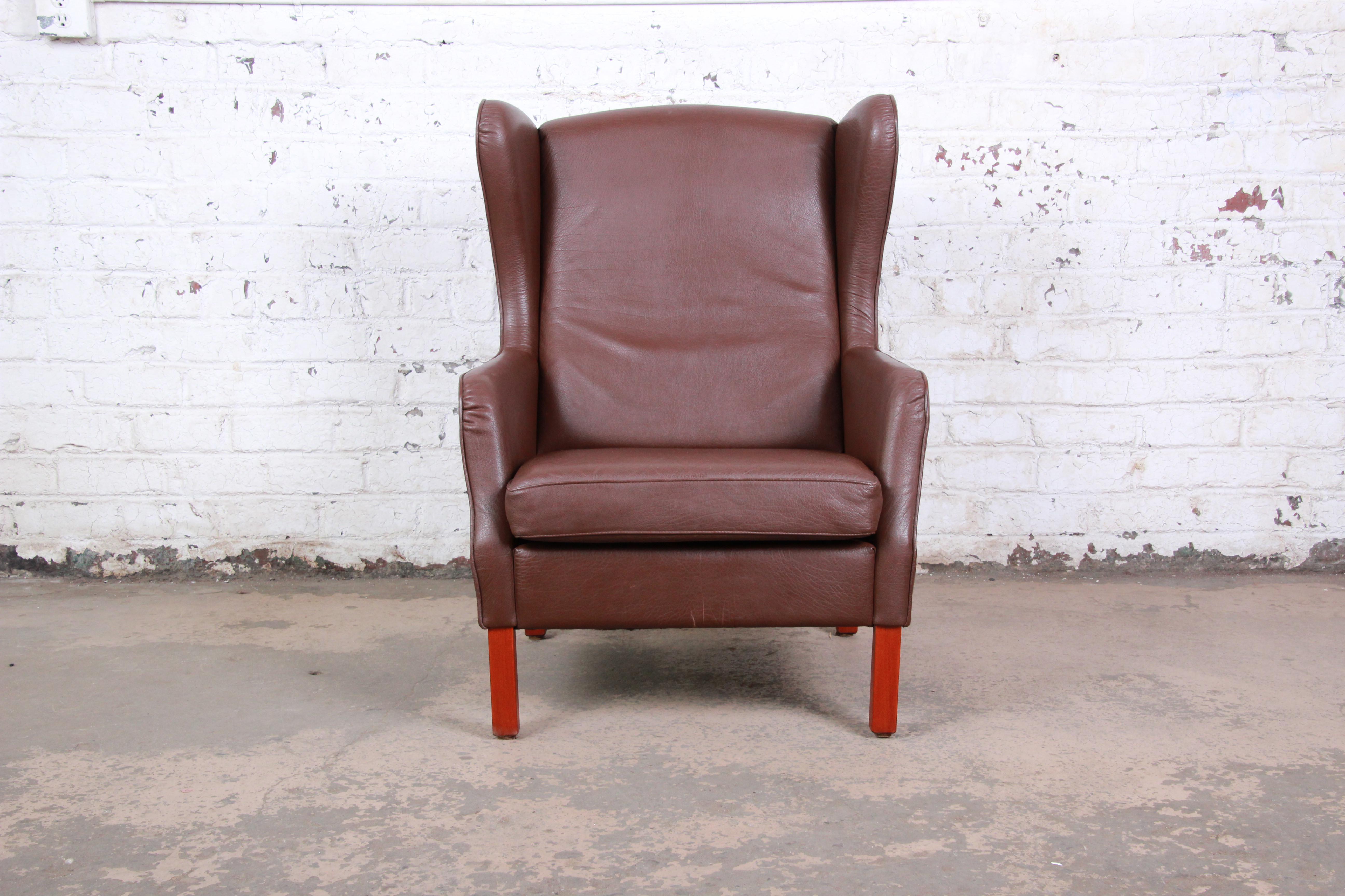 A gorgeous Danish modern brown leather wingback lounge chair in the style of Borge Mogensen. The chair is a wonderful blend of classic traditional and modern styles. It sits on squared mahogany legs. The chair is comfortable and overall in good