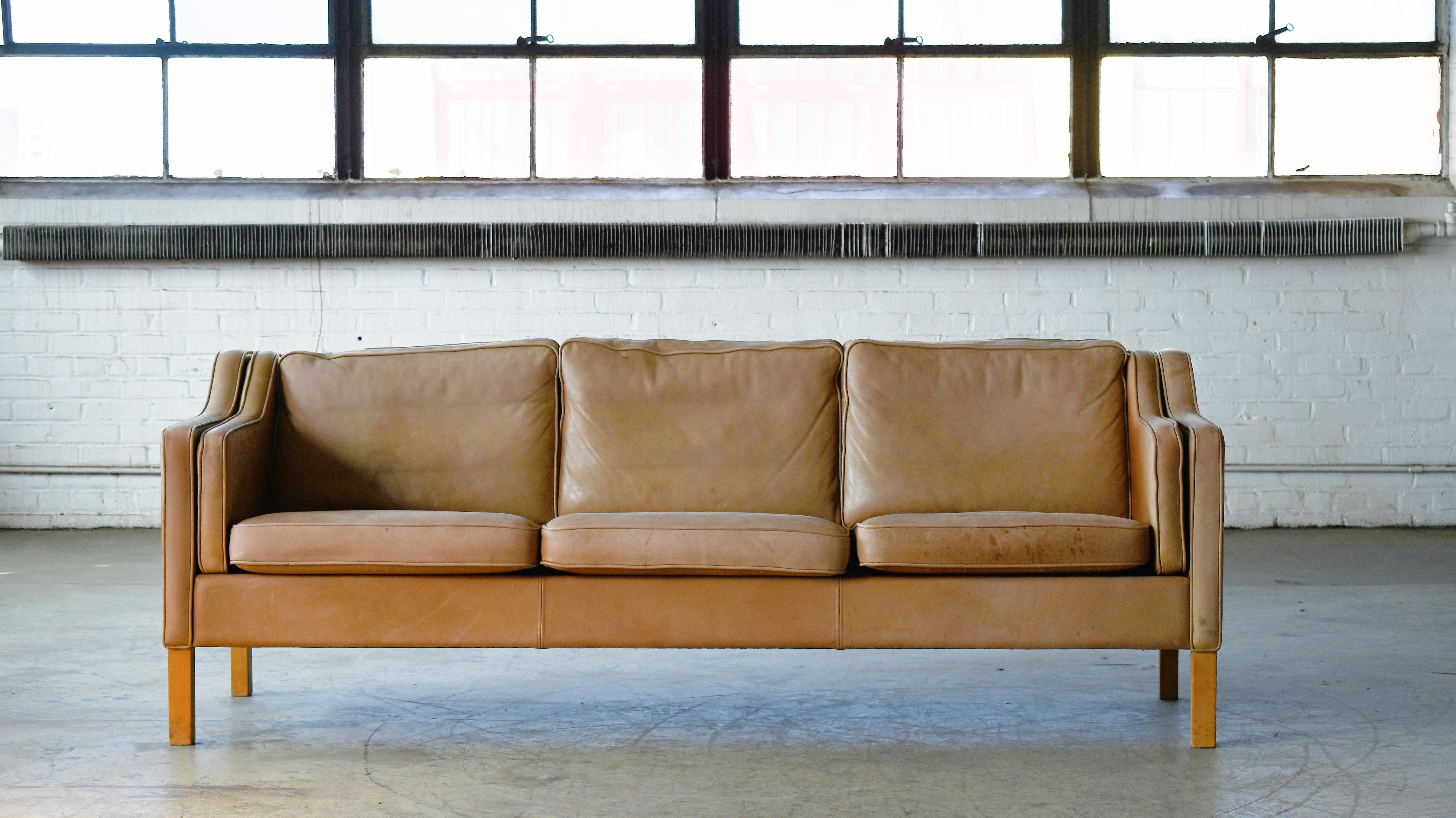 Classic Borge Mogensen style three-seat sofa in cognac leather by Stouby Mobler, Denmark. Cream or beige colored leather raised on legs of beech. High quality craftsmanship and overall very good condition showing some almost perfect natural age wear