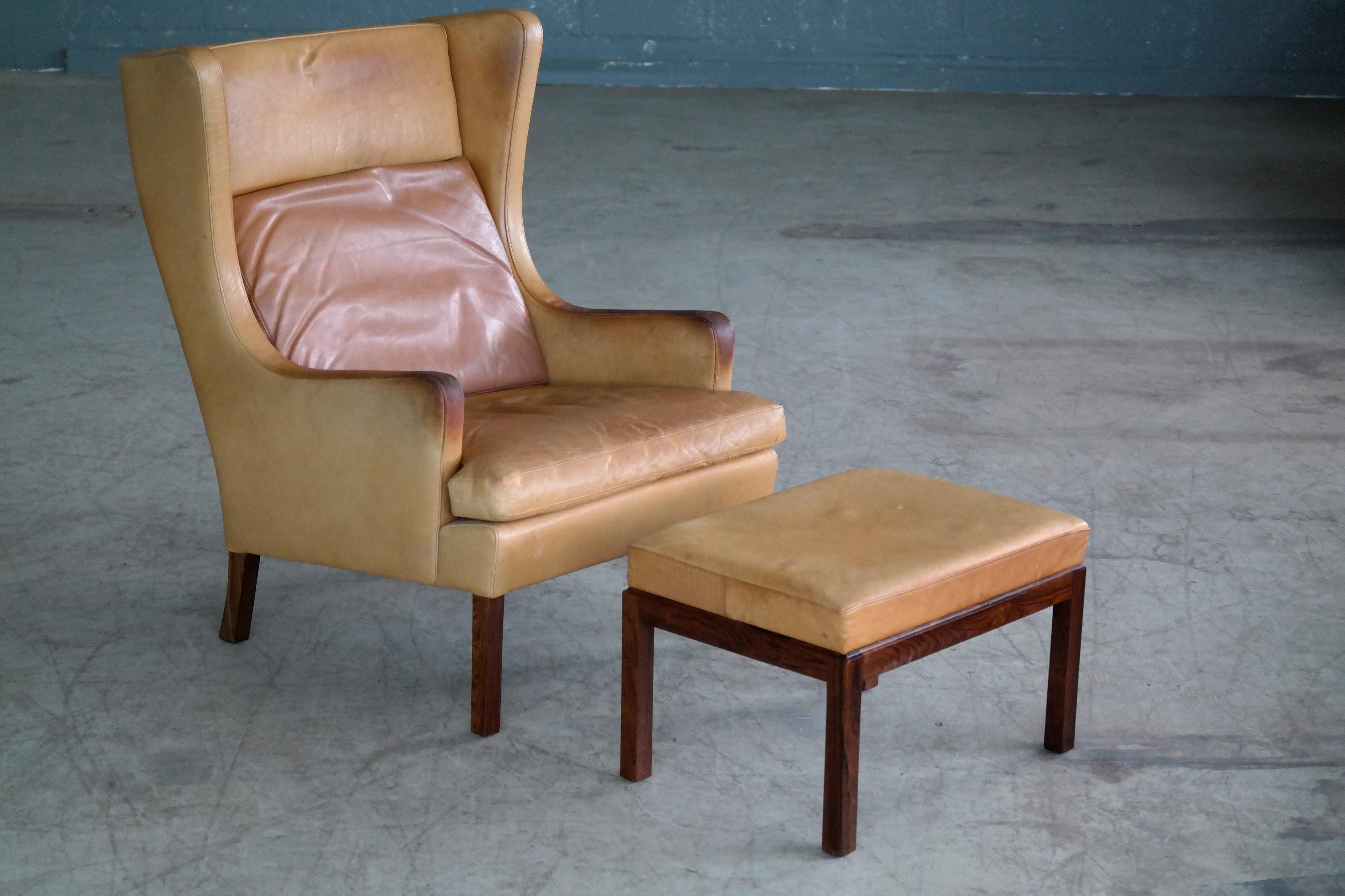 Very stylish Danish wingback lounge chair with ottoman in butterscotch leather raised on legs of rosewood. The butterscotch leather shows nice wear and patina with minor crazing to the top of the armrests. The rosewood legs and base with nice deep