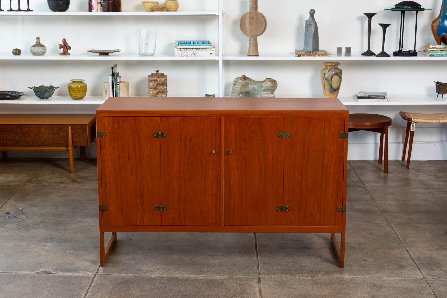 Børge Mogensen teak cabinet for Aalborg, Denmark, circa 1950s. The cabinet features a teak exterior frame and legs with white oak interior, patinated bronze hardware and folding door openings with adjustable shelving and drawers.

Condition: