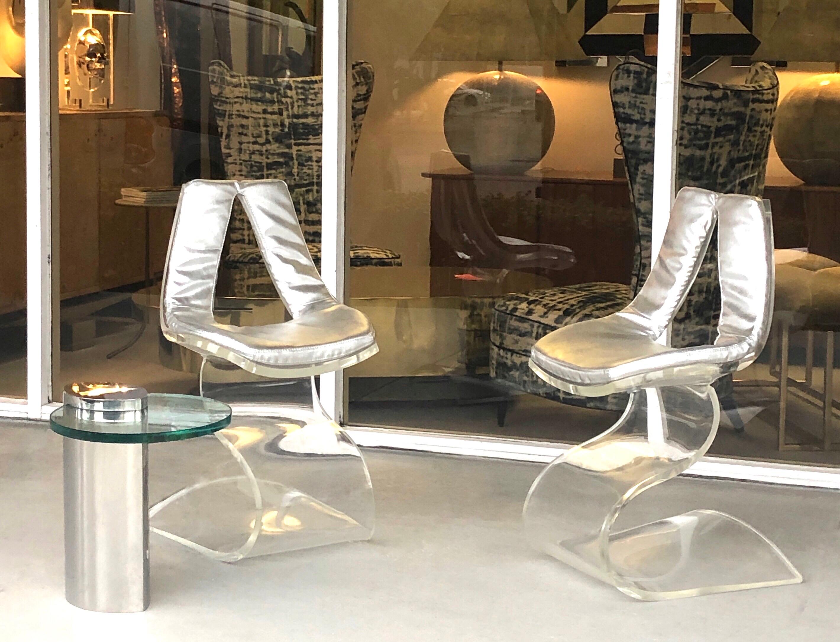 A wonderful pair of sculptural chairs. A single sheet of thick, clear Lucite manipulated into an artful practical piece of furniture. Retains the original silver faux leather upholstery.