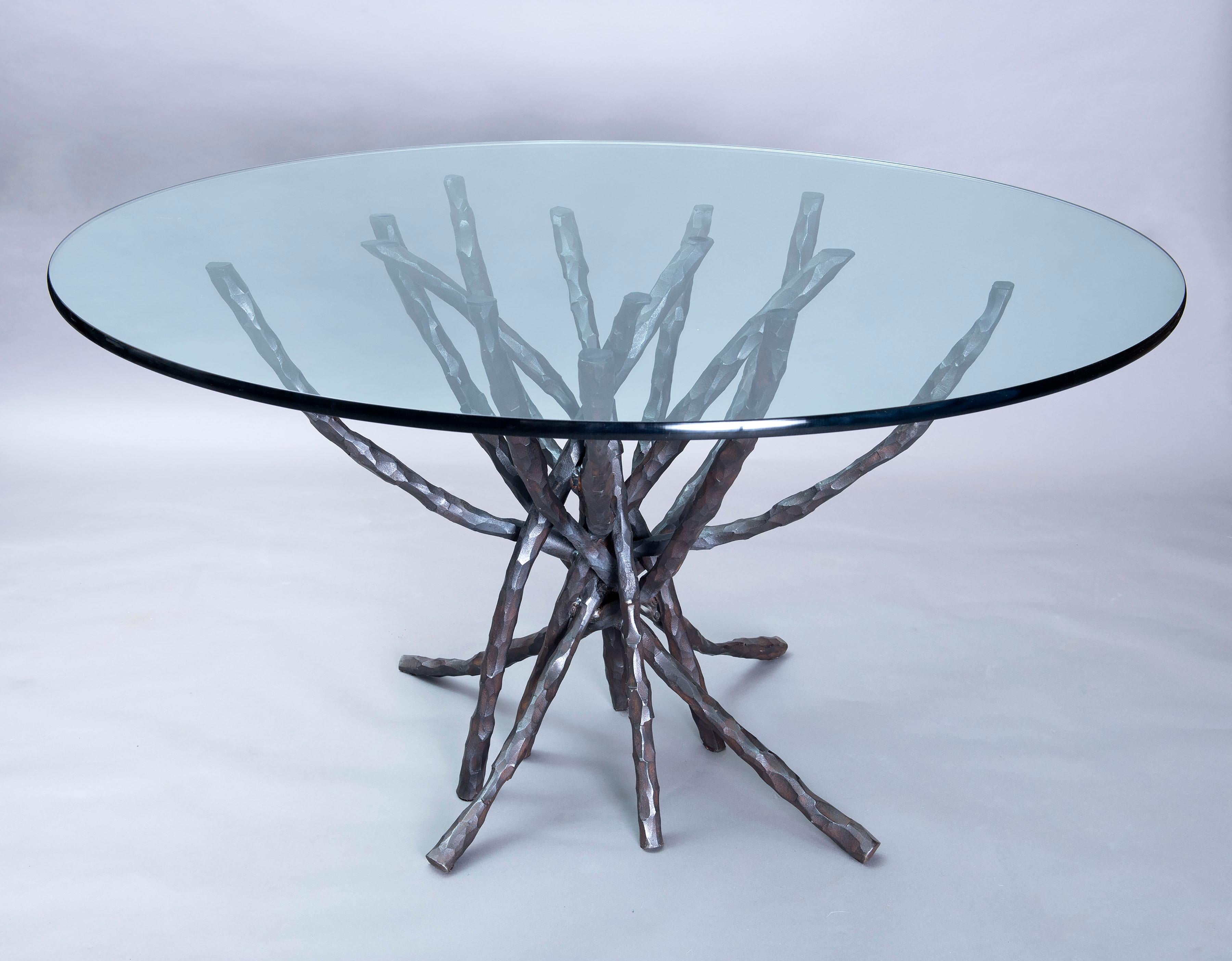 This one of a kind sculptural dining table in the round was handwrought from heavy solid bar stock. Heated and hammered and bent by hand each element is unique and welded in the center where the pieces intersect and coincide. The rich reddish brown