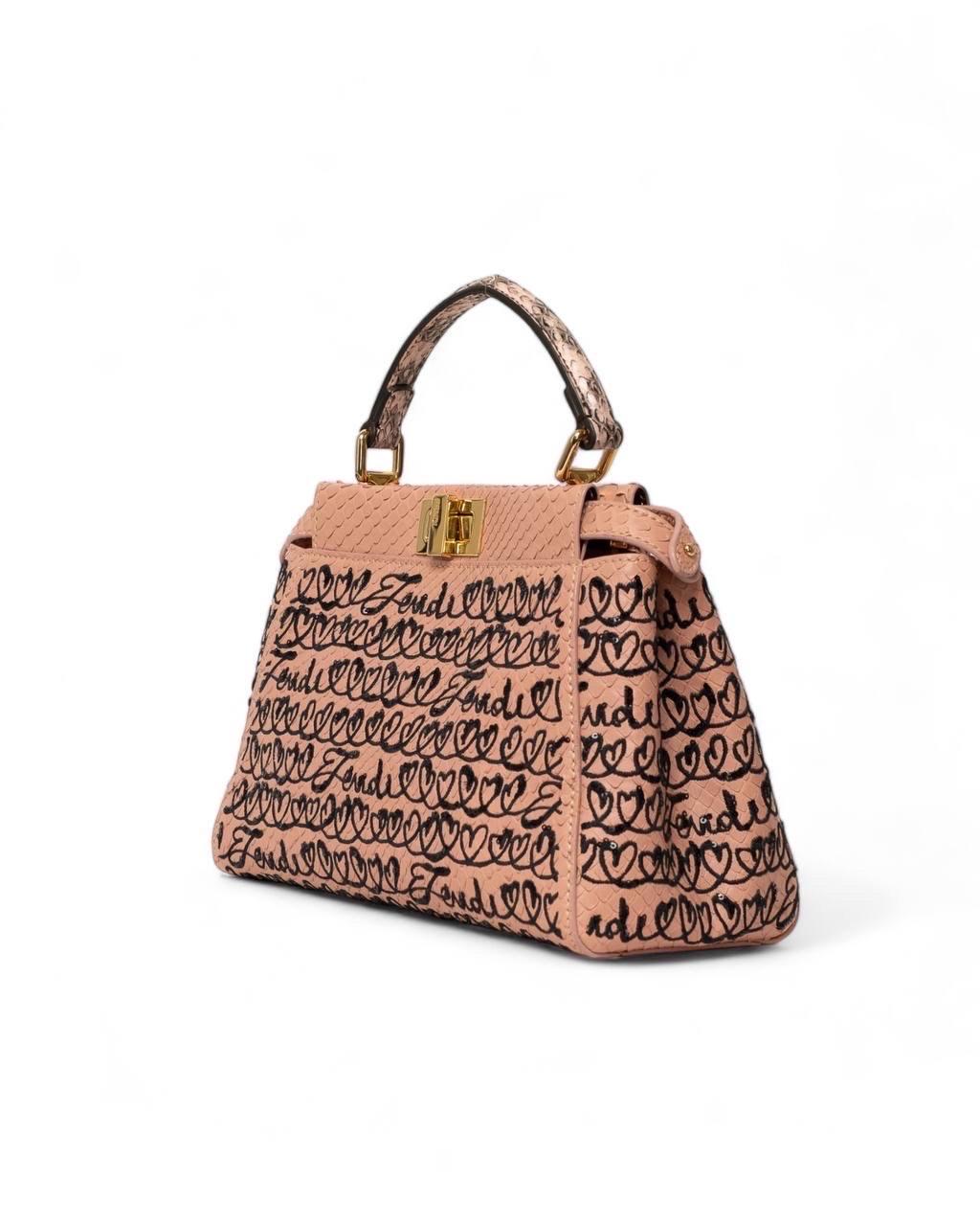 Borsa firmata Fendi, modello Peekaboo, misura mini, realizzata in pelle di pitone rosa, con ricami in rialzo neri con mini paillettes. Dotata di un manico centrale per portata a mano e di una tracolla sottile regolabile e rimovibile. Munita di
