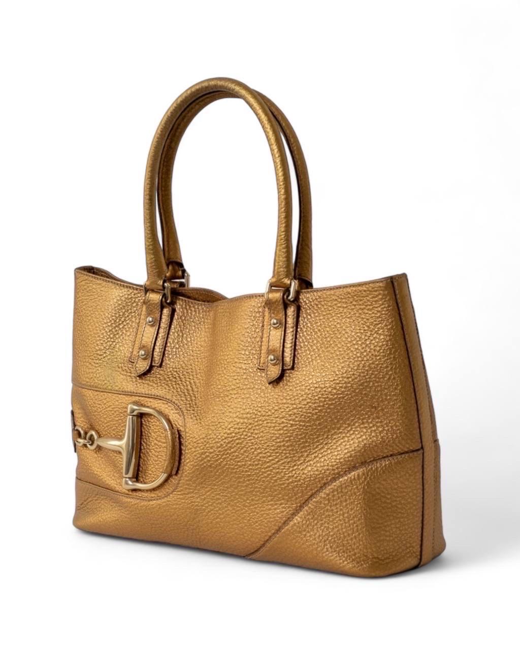 Borsa firmata Gucci, linea Horsebit, modello Hasler, realizzata in pelle martellata oro con hardware dorati. Doté d'une couture interne sur le fond calamiteux, d'une doublure interne en tissu marron et d'une fermeture à glissière, il est très léger.