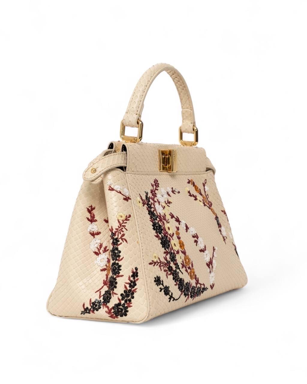 Borsa firmata Fendi, modello Peekaboo, misura mini, realizzata in pelle di pitone color panna con hardware dorati. Dotata di doppia chisura a girello fronte retro, internamente rivestita in pelle liscia marrone, capiente per l’essenziale. Munita di