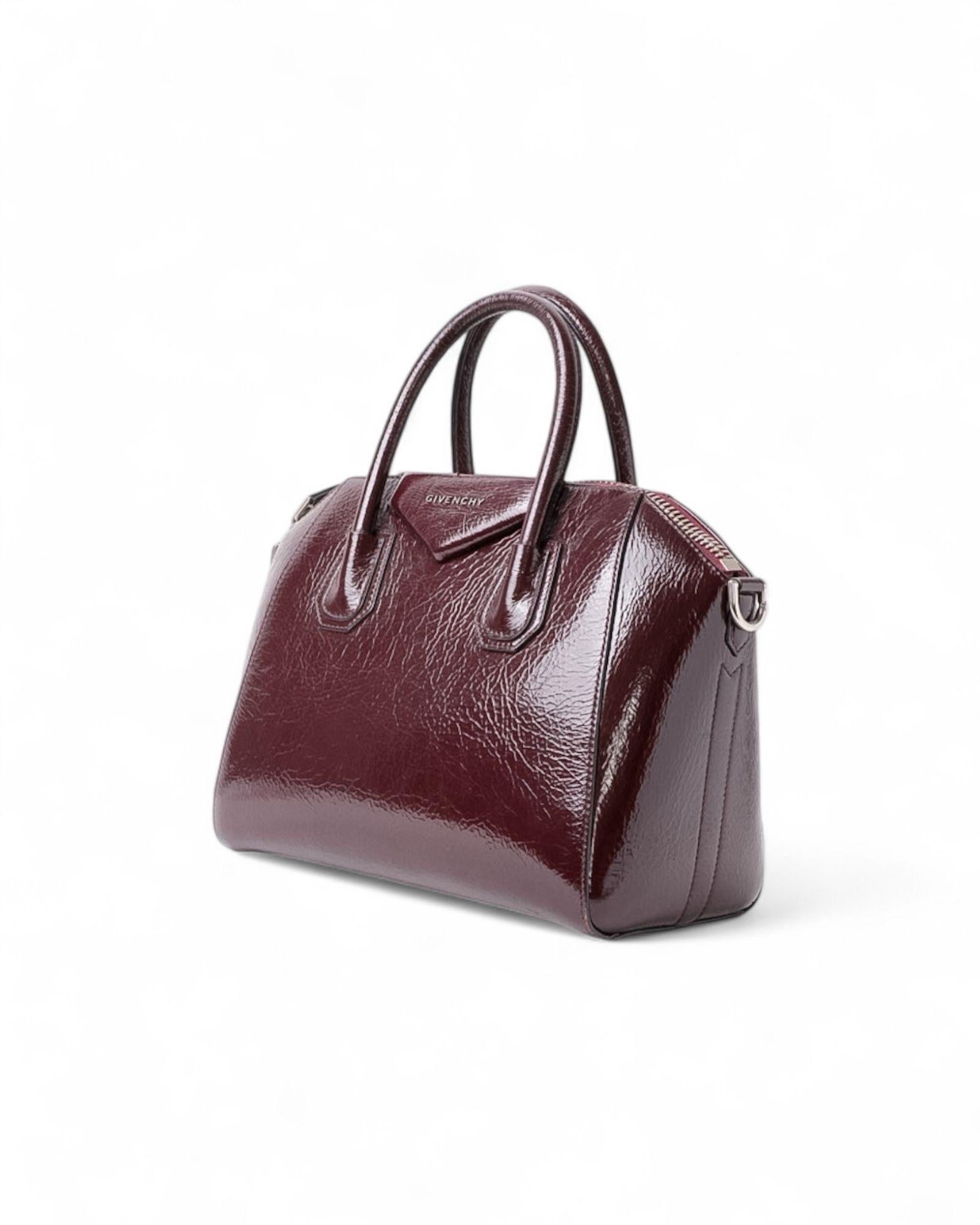 Borsa firmata Givenchy, modello Antigona, misura Small, realizzata in pelle lucida di un elegante color borgogna E hardware argentati. Dotata di chiusura superiore a zip, l’interno è rivestito in tela tono su tono e offre pratiche tasche, garantendo