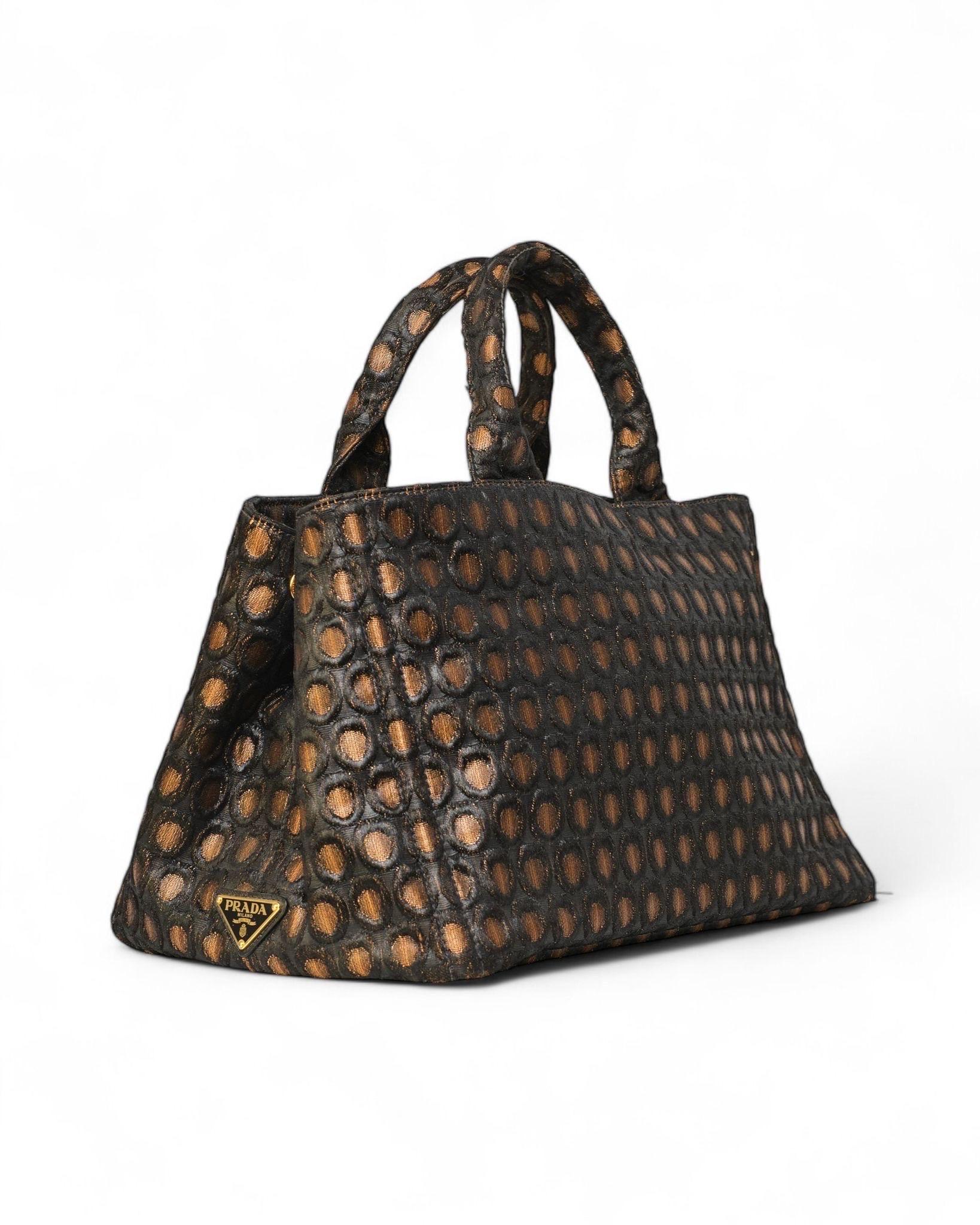 Borsa firmata Prada, modello shopper canapa, realizzata in tela nella fantasia circle nella colorazione marrone e nera con hardware dorati. Dotata di doppio manico superiore e di una tracolla rimovibile e regolabile, per una portata a spalla o a