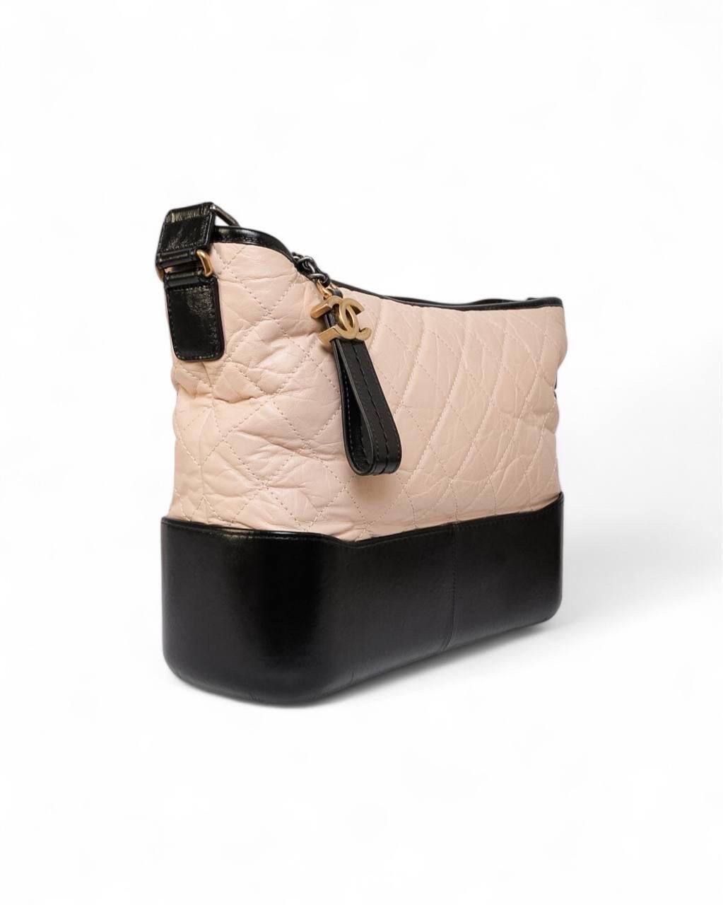 Borsa firmata Chanel, modello Gabrielle nella misura medium, realizzata in pregiata pelle nella colorazione cipria con rifiniture nere e hardware bicolor in oro e argento. La chiusura superiore a zip è adornata da un charm “CC”, mentre l’interno,
