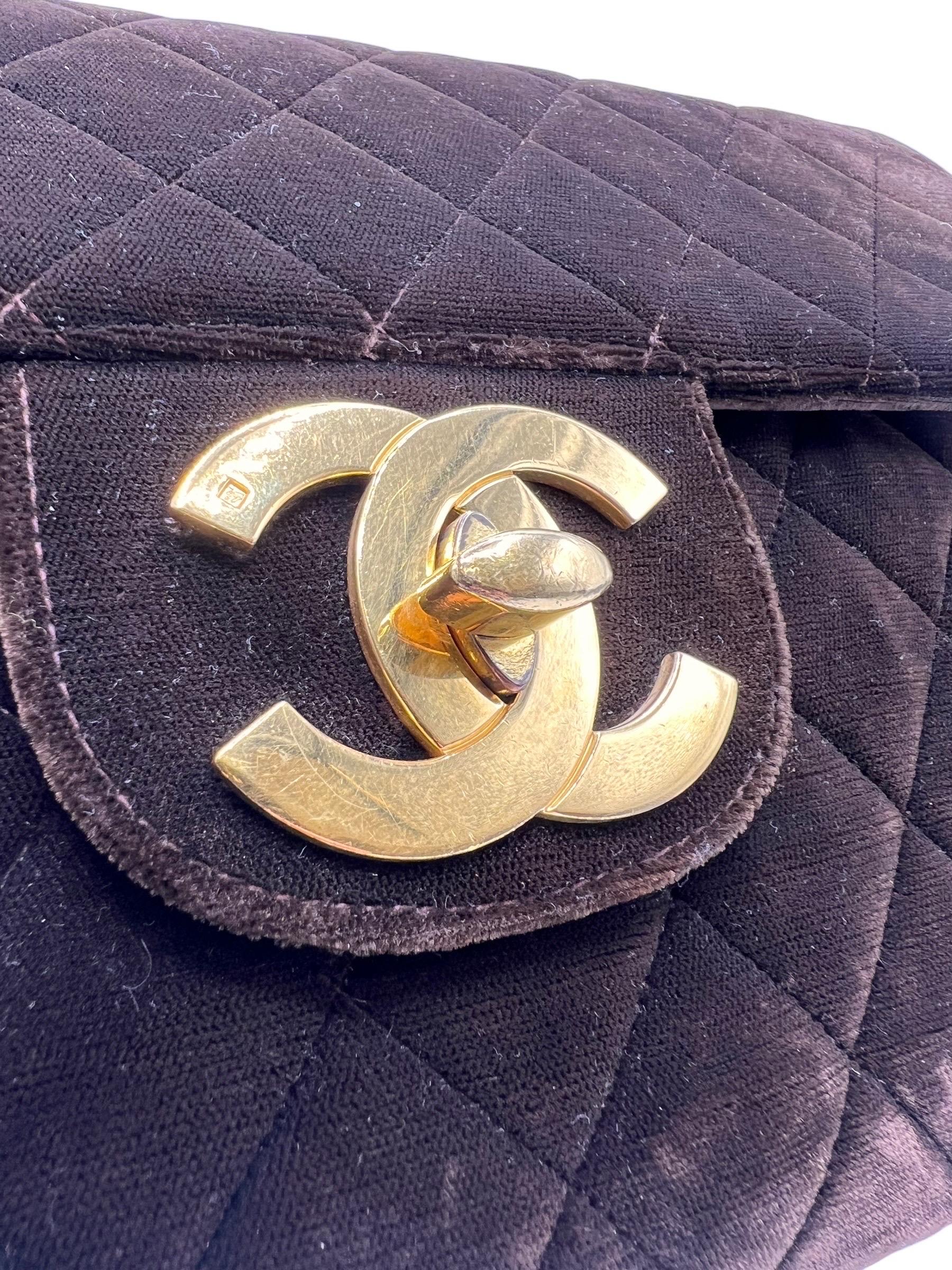 Borsa firmata Chanel, modello Jumbo Big Logo, realizzata in velluto marrone con hardware dorati. Dotata di chiusura a girello e classico logo CC, internamente rivestita in pelle liscia marrone, abbastanza capiente. Munita di una tracolla a