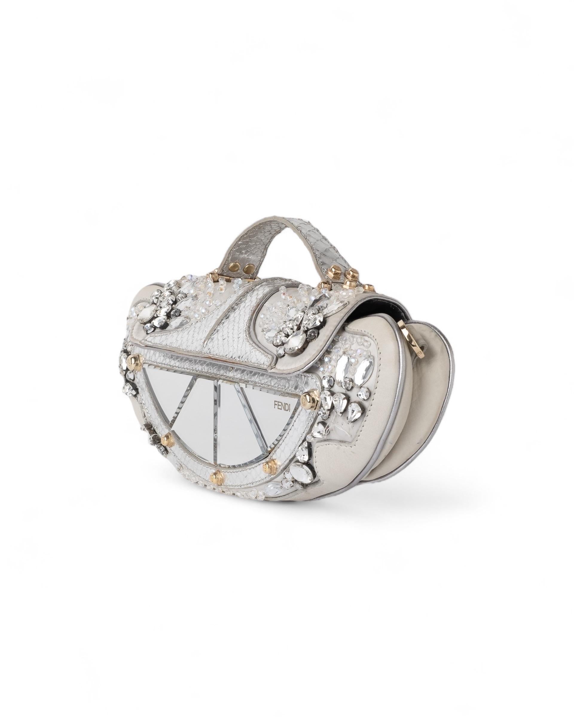 Borsa firmata Fendi, modello Vanity Mirror, realizzata in raso color ghiaccio con interni in finta pelle pitonata e hardware dorati. Dotata di una patta con chiusura ad incastro, internamente rivestita in raso grigio, capiente per l’essenziale.