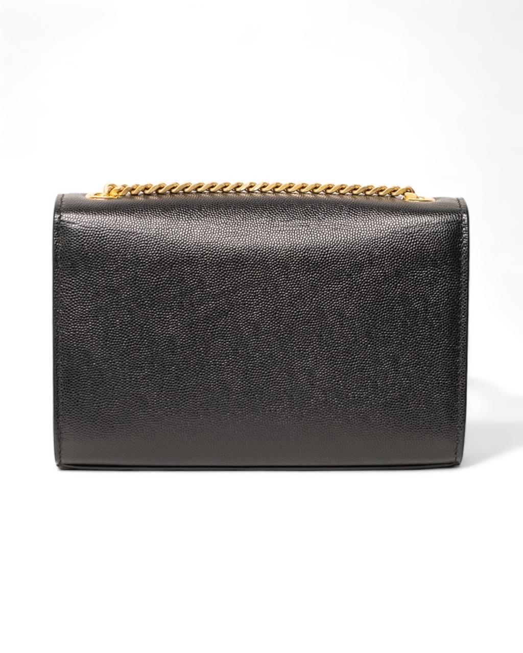 Borsa firmata Saint Laurent, modello Kate, misura Small, realizzata in pelle granulata nera con hardware dorati. Dotata di una patta frontale con chiusura a bottone calamitato, internamente rivestita in tela tono su tono, capiente per l’essenziale.