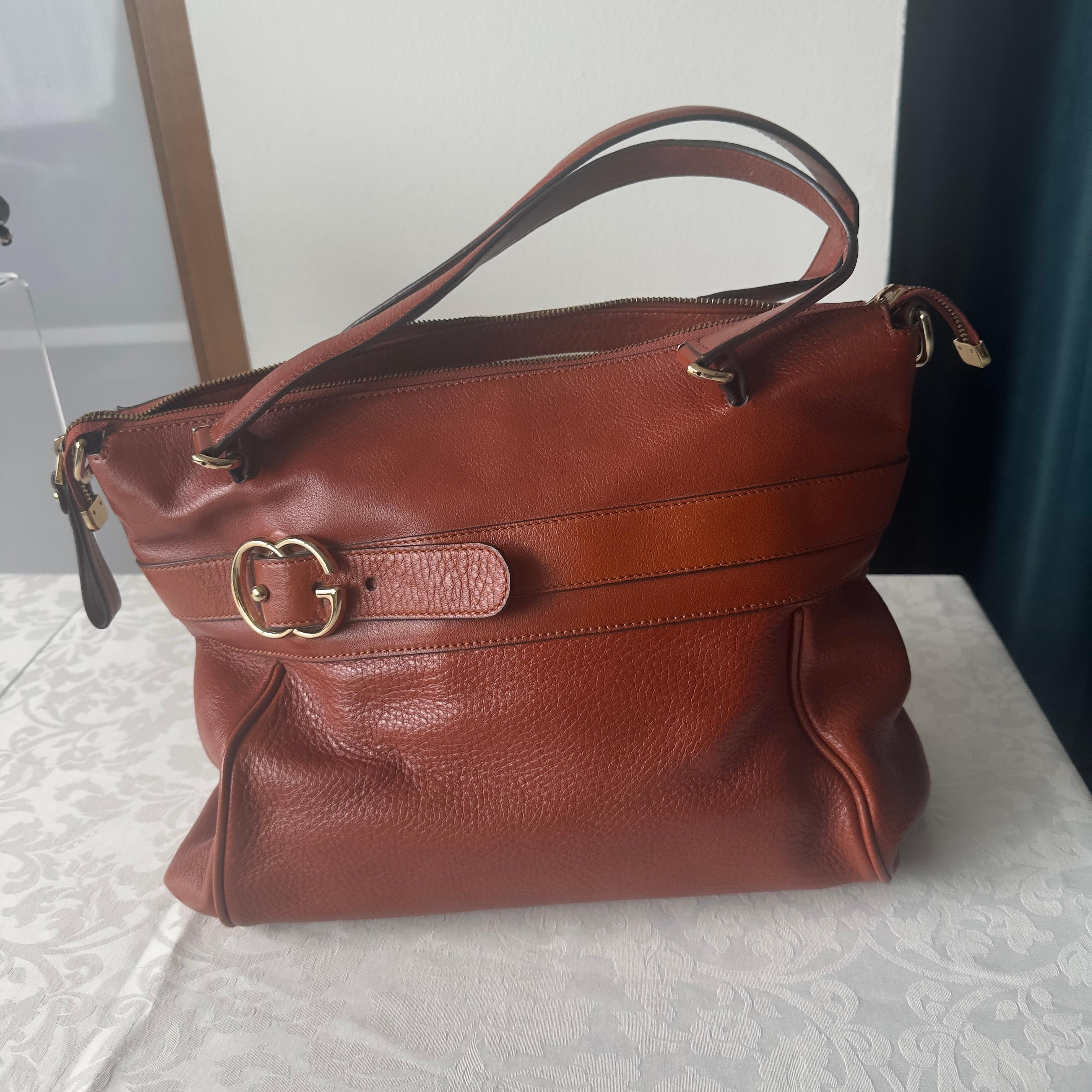 Gucci biscuit-colored leather bag with G buckle in the front 
Double-slider zipper closure, two handles, fabric interior with breast pocket 
Equipped with two side hooks for adding shoulder strap 
To be carried on the arm or over the shoulder 
Like