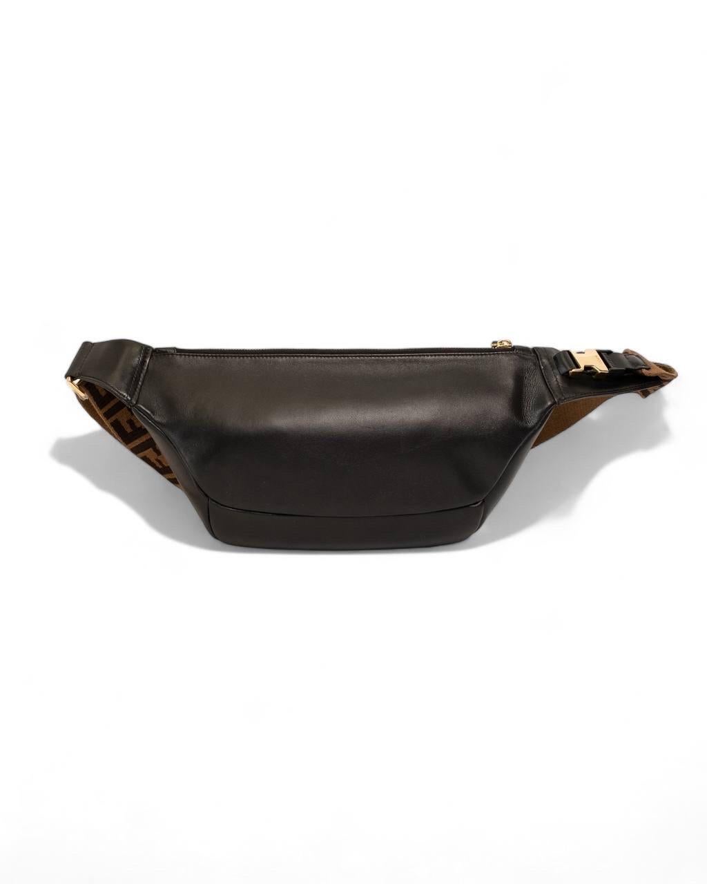 Marsupio firmato Fendi, modello Belt Bag, realizzato in pelle liscia nero con hardware dorati. Dotato di una chiusura superiore a zip, internamente rivestito in tela tono su tono, capiente per l’essenziale. Munito di una tracolla in tessuto marrone