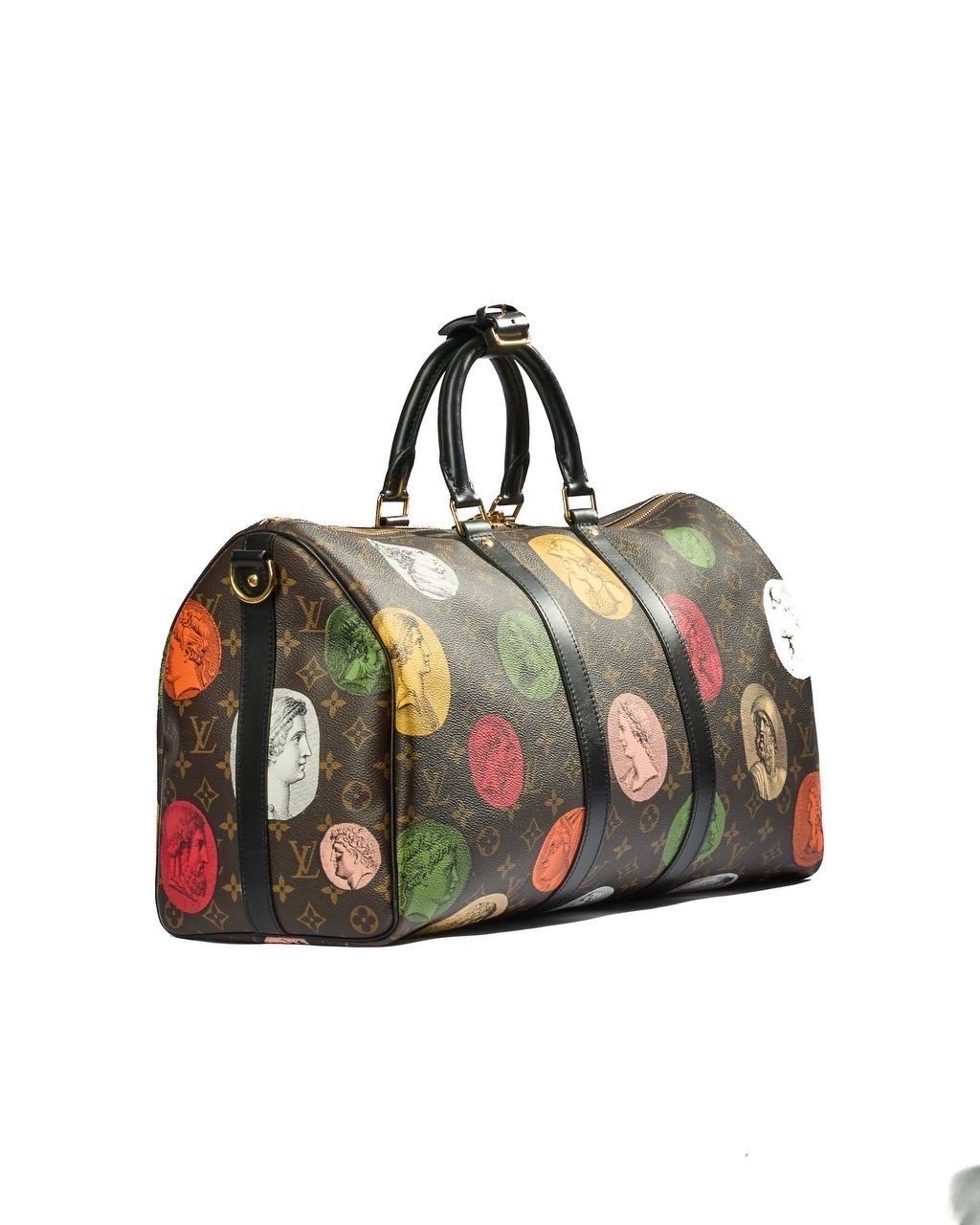 Borsa firmata Louis Vuitton, modello Keepall Bandoulière, misura 45, in edizione limitata della collezione Fornasetti. Realizzata in tela monogram con dettagli in macassar nero e hardware dorato, questa borsa è un vero pezzo da collezione. Munita di