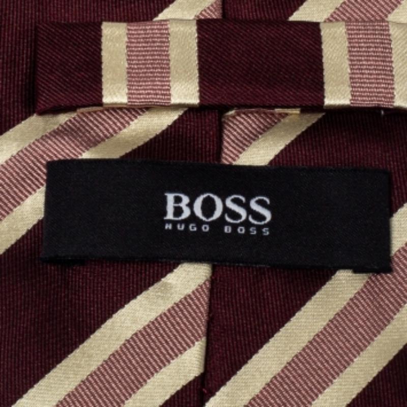 This Boss By Hugo Boss tie is a perfect formal accessory that has a sharp and modern appeal. Made from 100% silk, it features a burgundy shade, striped pattern, a penny keeper strap, and the brand label neatly stitched at the back. It is sure to add