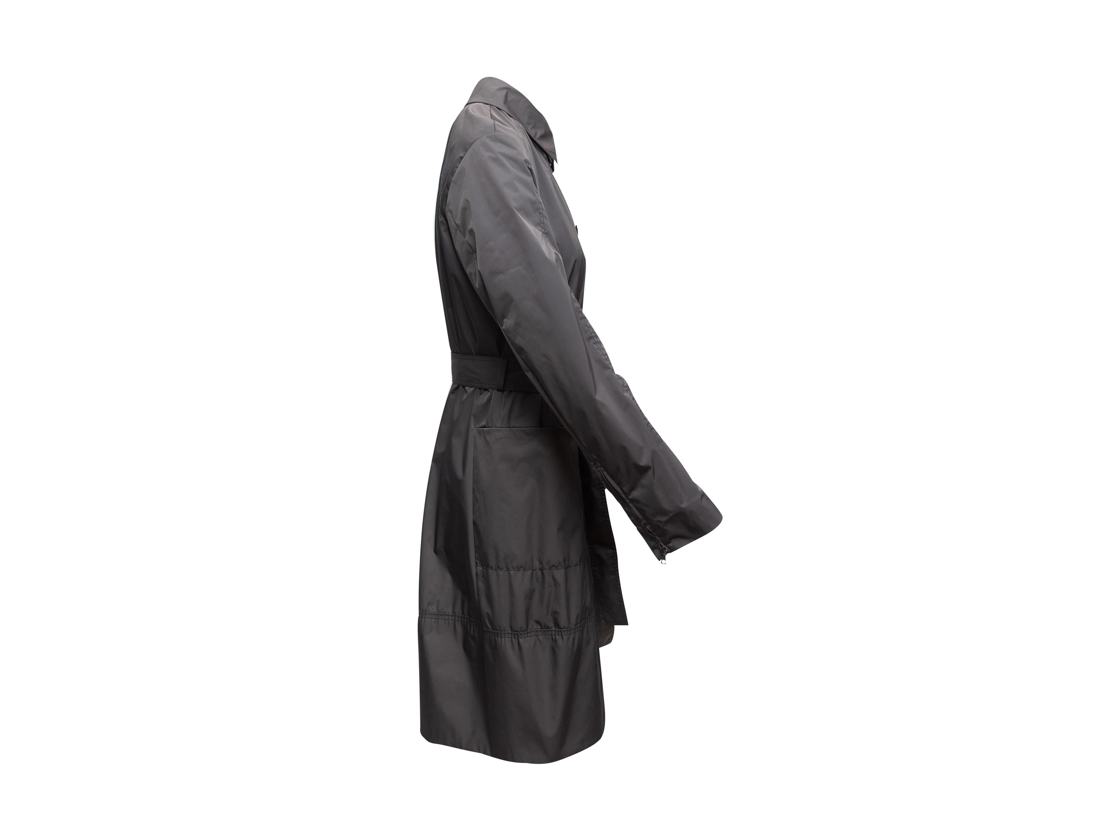 Product details: Charcoal grey nylon trench coat by Boss. Pointed collar. Dual hip pockets. Sash tie at waist. Button closures at center front. 40
