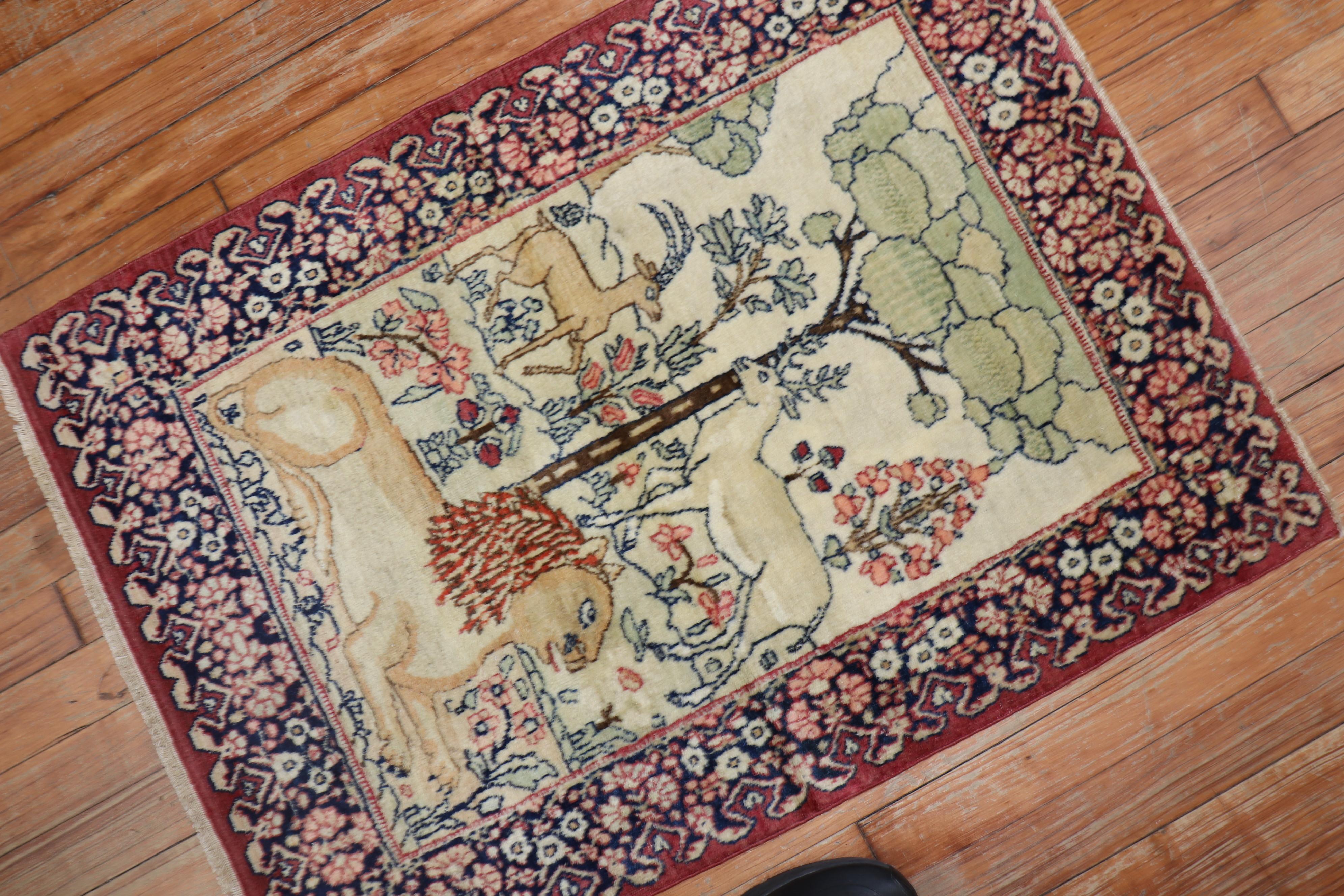 An early 20th century Persian Lavar Kerman pictorial rug with a lion, deer and goat covering a scenic forest scenery. The field ivory, the border is a rosy red. The traditional colors are seen in many lavar Kerman rugs. The weave on this is fine.