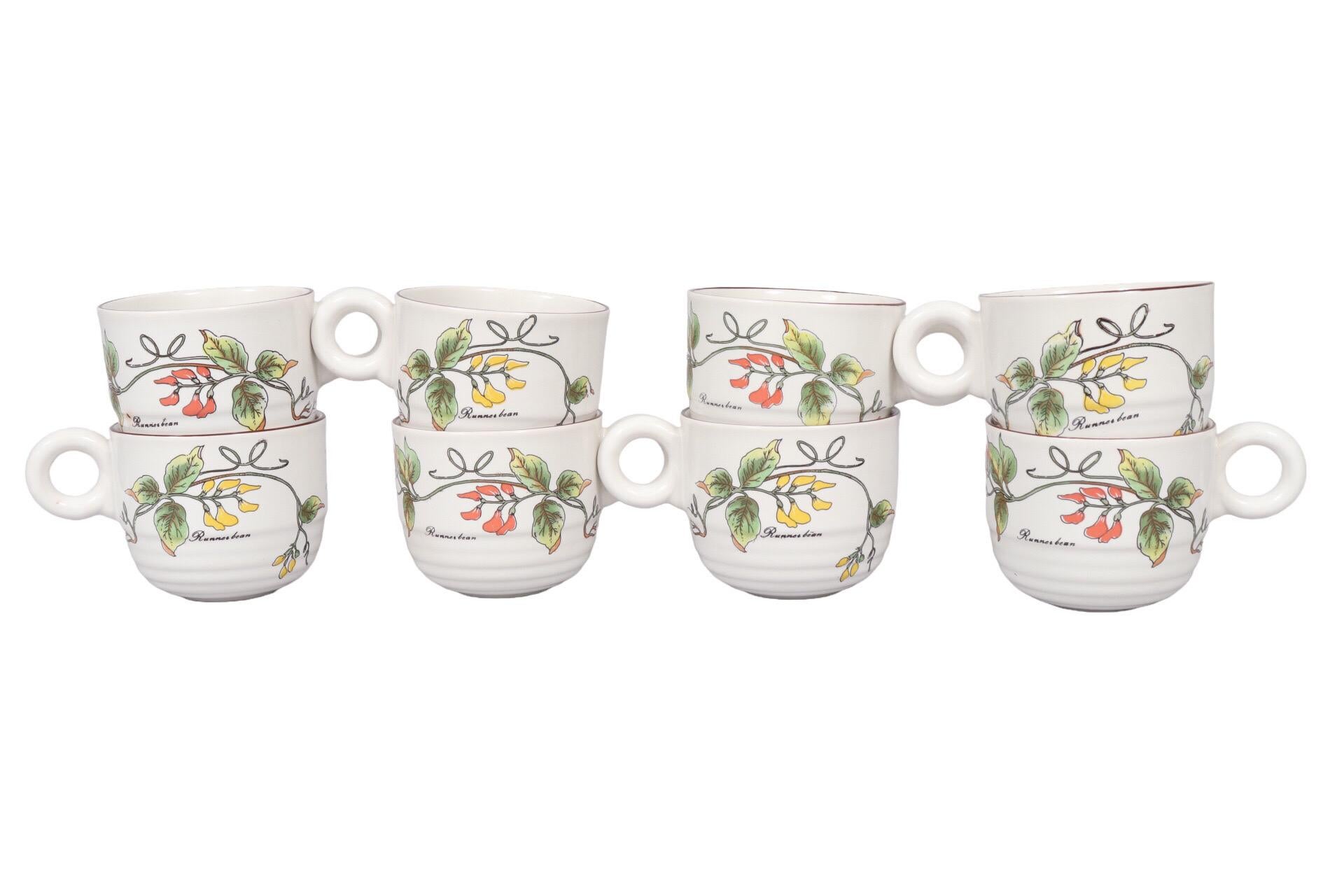 A set of eight ceramic coffee or tea cups. Decorated on each side with trailing runner bean vines flowering in red and yellow, the words “runner bean” below in cursive script. Cups have small round handles and undulating beveled bases. Marked