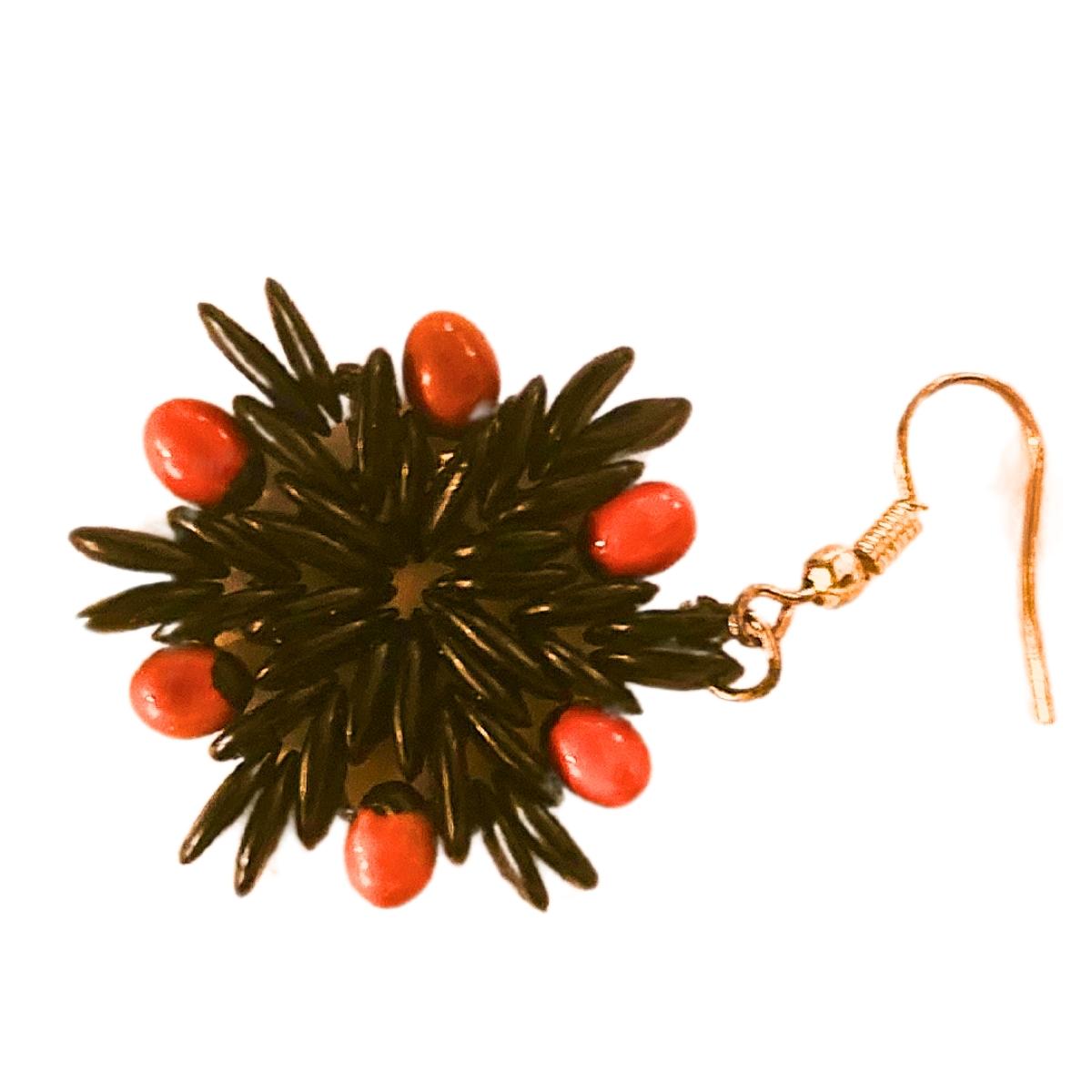 The Midnight Flame Earrings are a bold and striking fusion of deep black-dyed wild tamarind seeds and vibrant red jumbie beads. The star-like arrangement of the tamarind seeds creates a captivating central design, while the fiery red jumbie beads
