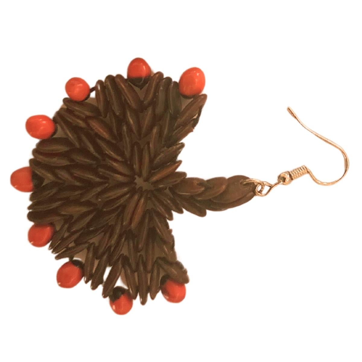 Gli orecchini Scarlet Edge Bloom combinano il fascino naturale dei semi di tamarindo selvatico con la vivacità delle perline jumbie rosse, creando un accessorio dinamico e accattivante. I ricchi semi di tamarindo marroni formano un motivo a stella