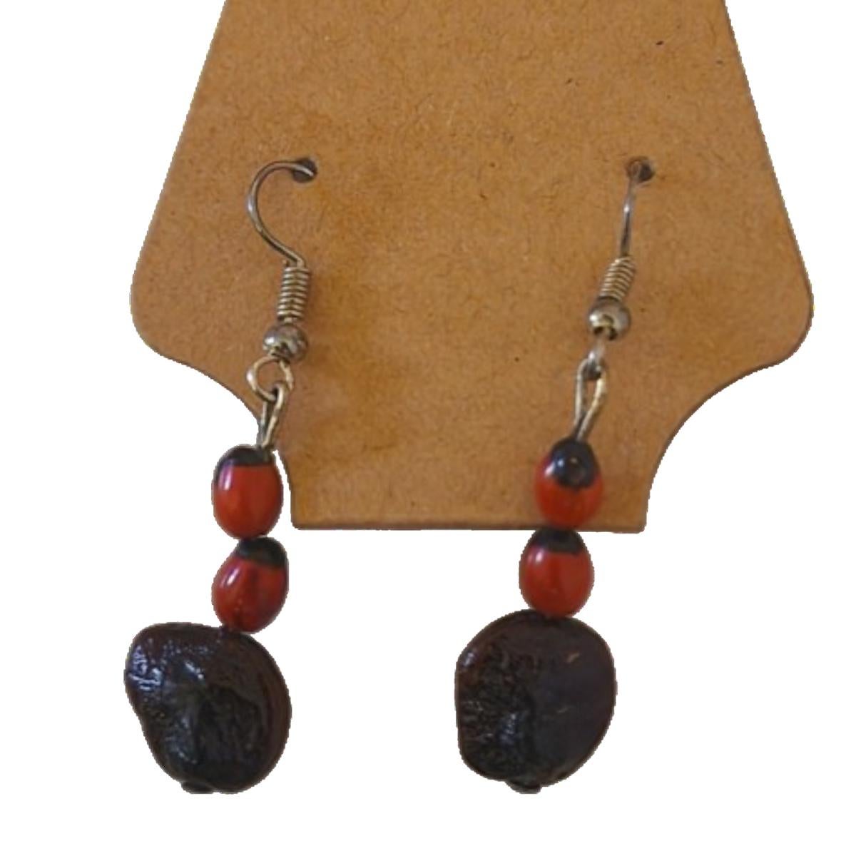 The Tamarind Gem Earrings are a perfect blend of simplicity and natural beauty, combining a single rich brown tamarind seed with two vibrant red and black jumbie beads. The tamarind seed, with its earthy texture, serves as the base of this
