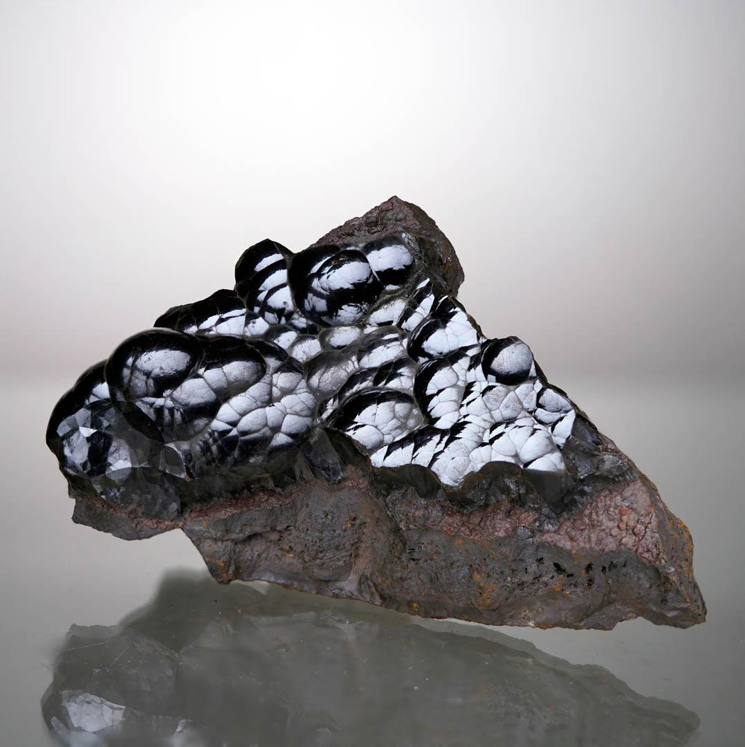 Questo straordinario esemplare di ematite proveniente dal Marocco mostra una brillante lucentezza naturale a specchio sui contorni fluidi e arrotondati della struttura cristallina botrioidale. La forma scultorea e la densità di questo pezzo gli
