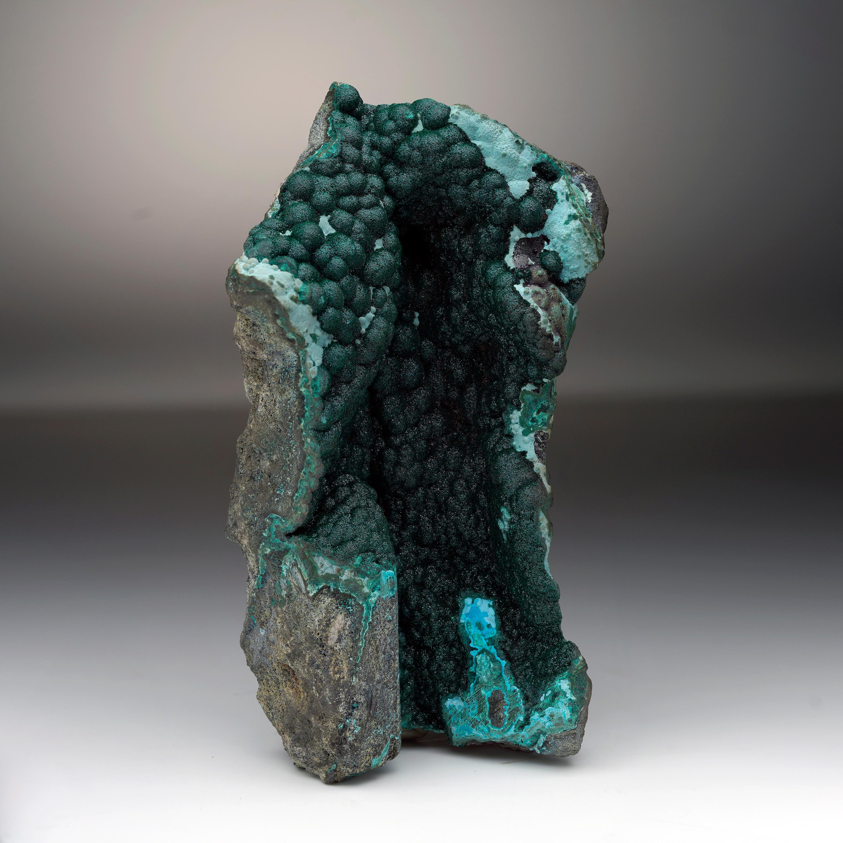 The velvety, druze-coated interior of this vug or natural crystal-lined rock crevice is filled with an abundance of beautifully formed deep emerald green botryoidal malachite crystals. The piece holds a dynamic, sculptural form echoed by the