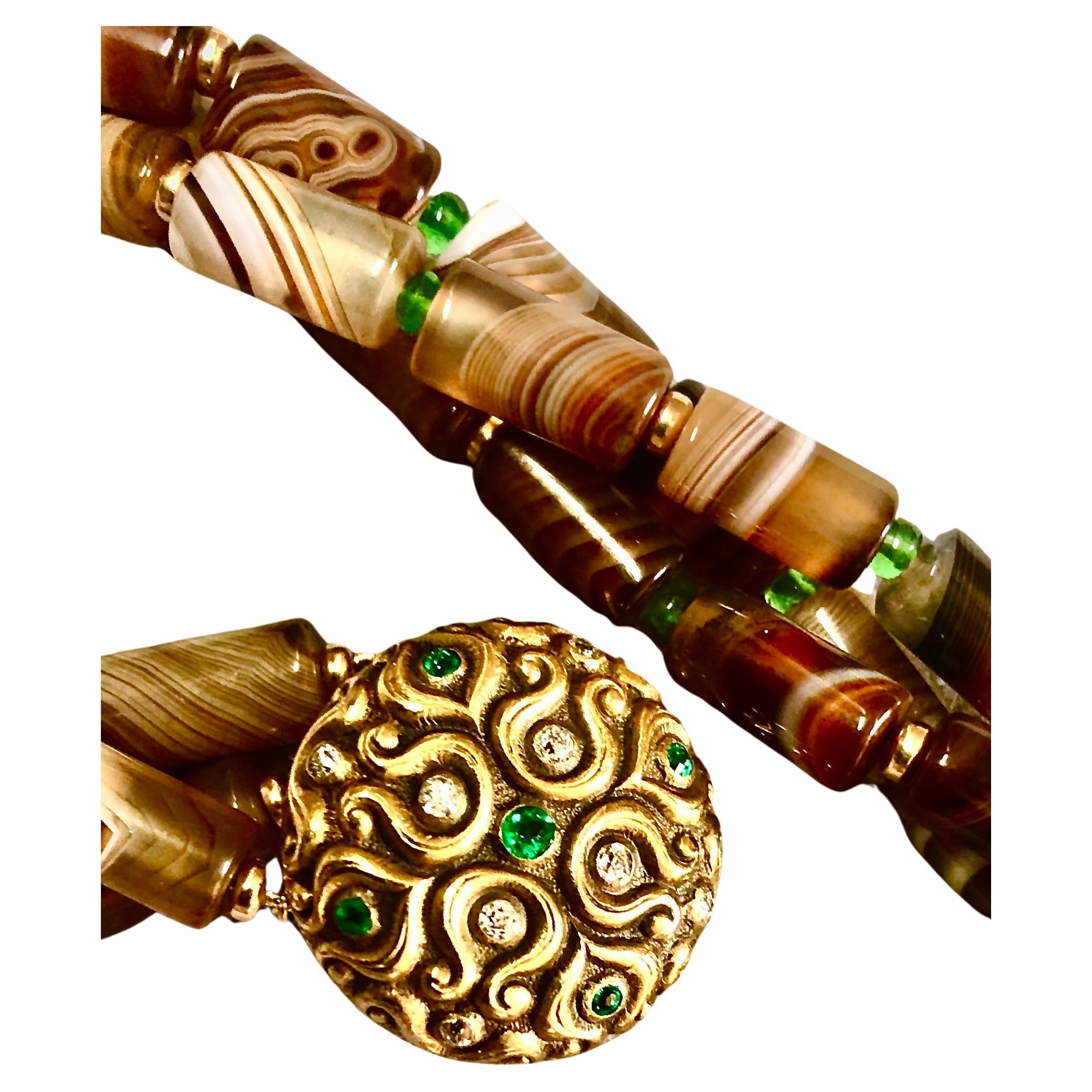 Handsome triple strand necklace of fascinating patterns of brown and caramel colored Botswana agate. The agate tubular beads are alternately place smooth rondelles of green tsavorite garnets and 14kt polished gold.

The focus of the beads is a