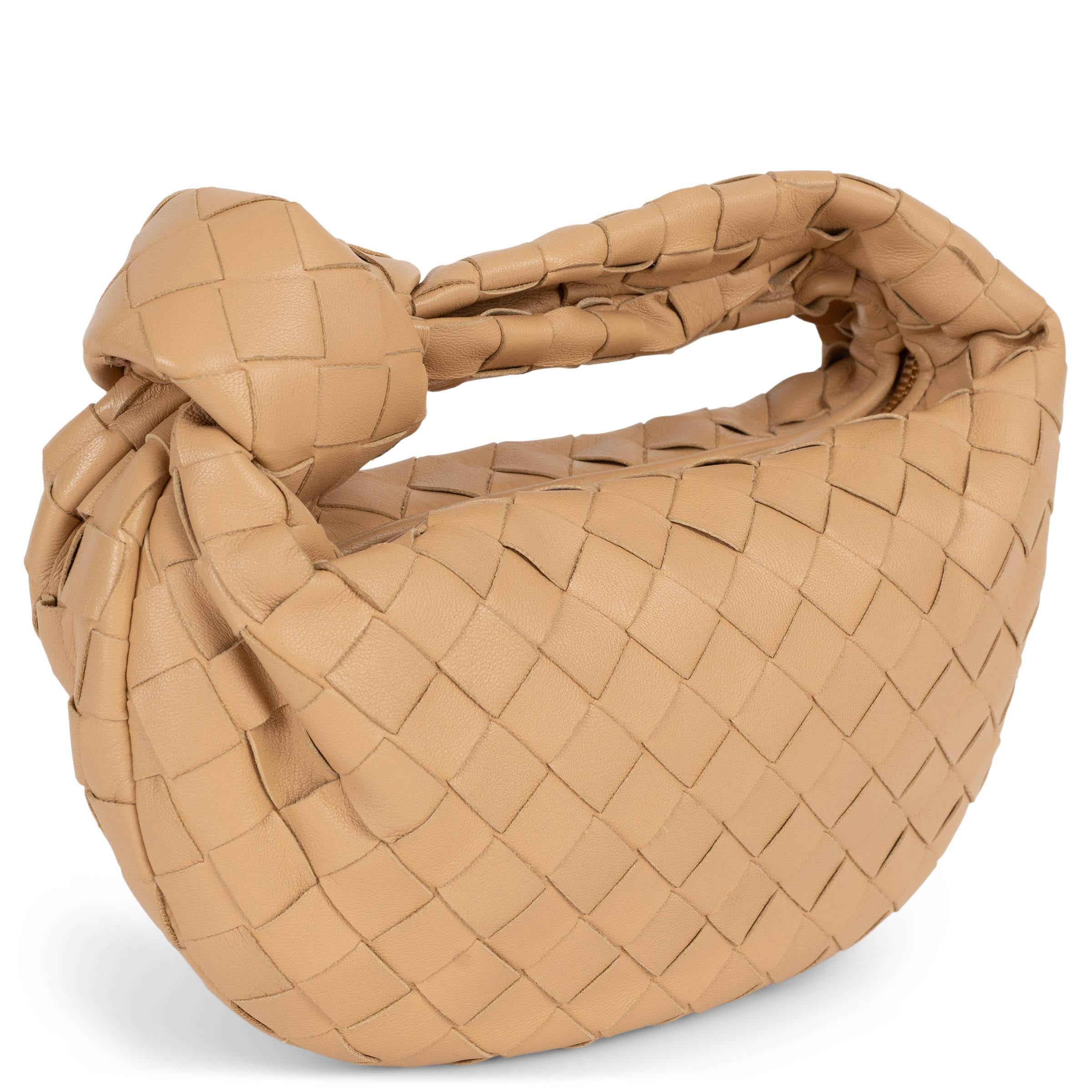 This 100% authentic Bottega Veneta Mini Jodie bag is crafted in Almond beige Intrecciato leather. It features the signature hobo silhouette with a distinctive knotted handle and opens with a top zipper. Lined in smooth leather, it's a compact yet