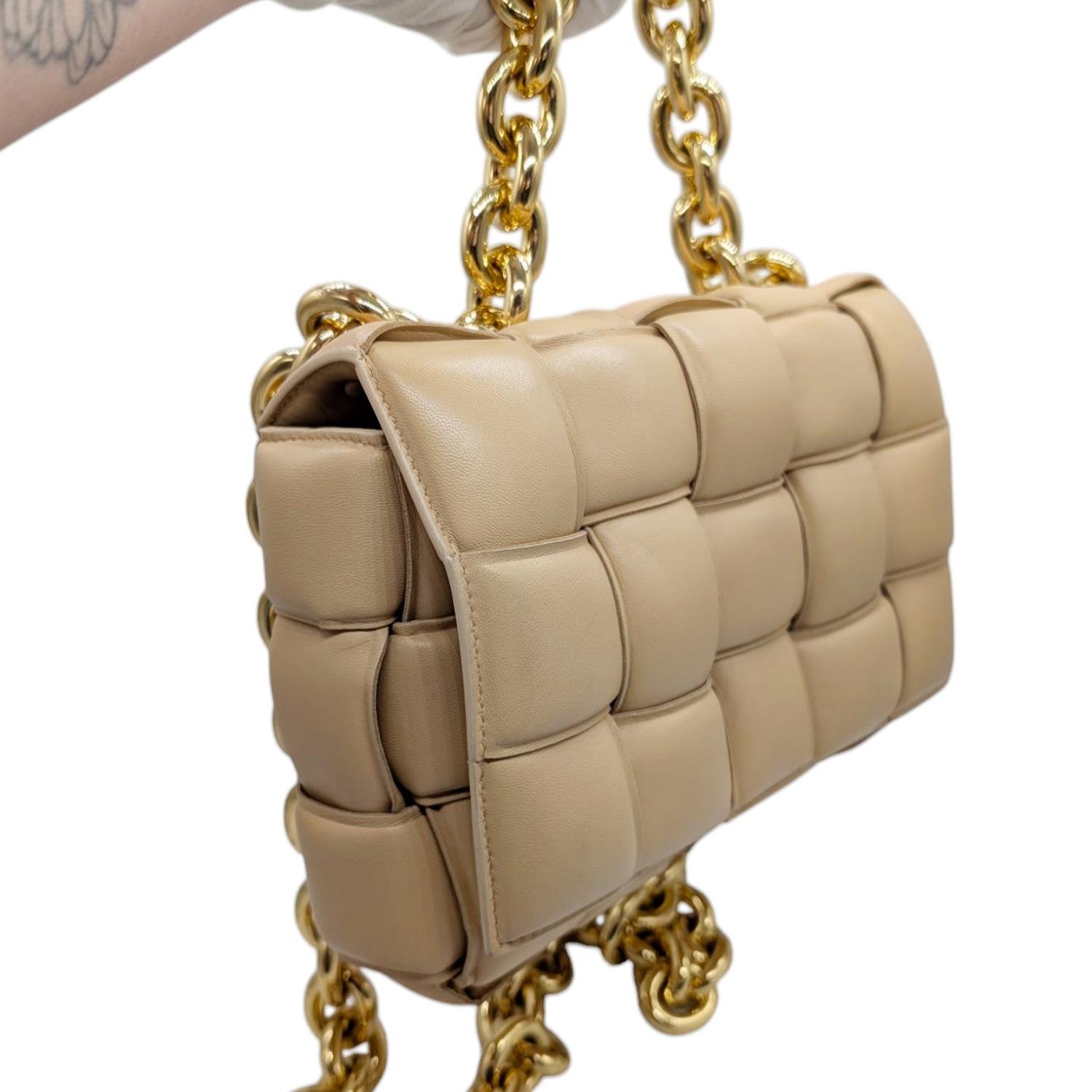 Ce sac à bandoulière Bottega Intreccio en cuir d'agneau matelassé est réalisé en cuir d'agneau tissé matelassé de couleur beige. Le sac est doté d'une bandoulière en chaîne dorée et d'une courte poignée en chaîne. Le rabat croisé s'ouvre sur un