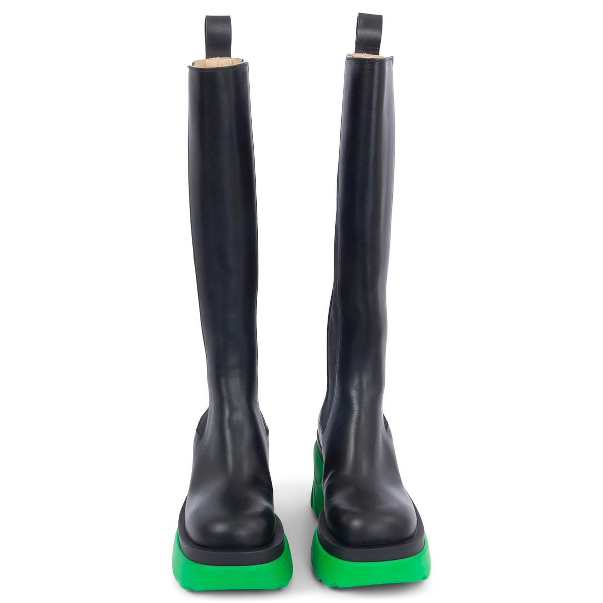 100% authentische kniehohe Bottega Veneta Flash-Stiefel aus schwarzem Kalbsleder mit einer klobigen, sittichgrünen Sohle mit flammenartigen Rillen, die von Supercars inspiriert ist. Das Design kommt mit elastischen Seitenfalten, einer Zuglasche an