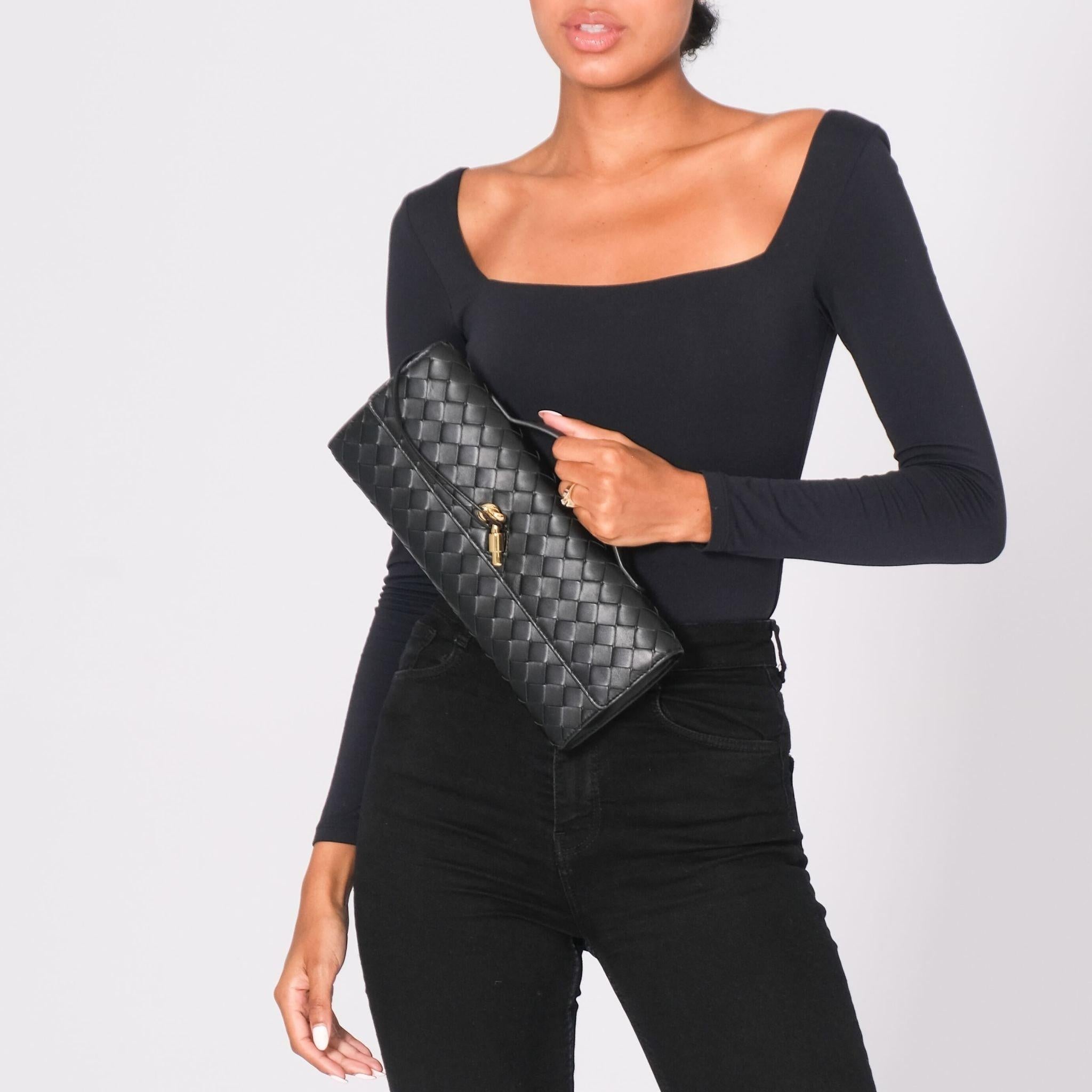 The Bottega Andiamo clutch bag is constructed from soft, supple lambskin leather and boasts several signature elements. The bag features intrecciato leather, a metallic knot closure, a top handle, a front flap, and brass-finished hardware in a light