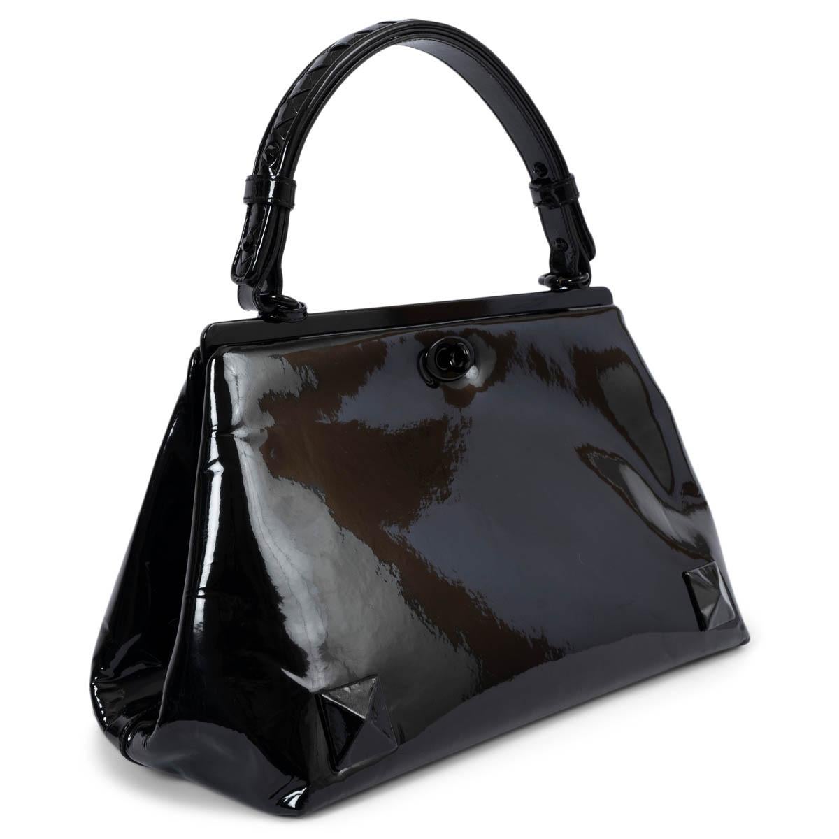 100% authentic Bottega Veneta top handle bag in black patent leather. Features a intrecciato woven handle, pyramid studs in the bottom corners and shiny black hardware. Opens with a turn-lock on each side into a cream interior with a zipper pocket