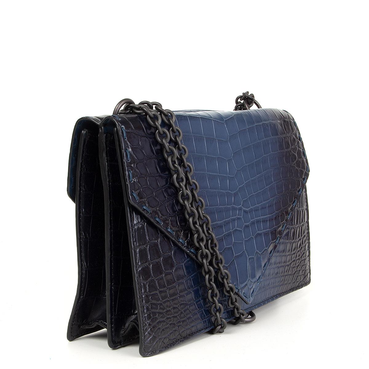 100% authentic Bottega Veneta envelope style double sided shoulder bag in navy and midnight blue crocodile. Opens with two magnetic buttons under the flap and is lined navy smooth calfskin with one zipper pocket against the back. Comes with a dust