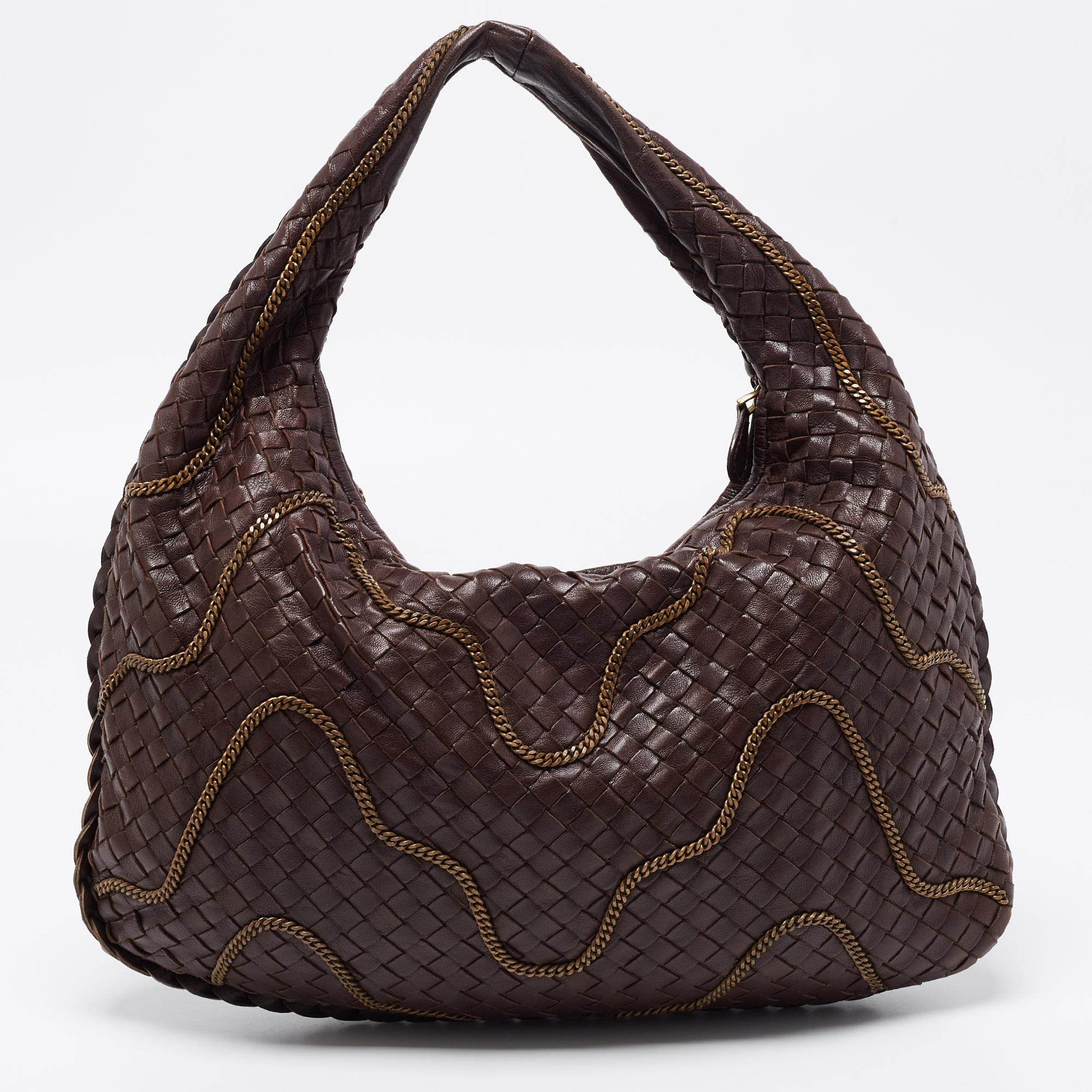 The excellent craftsmanship of this Bottega Veneta hobo ensures a brilliant finish and a rich appeal. Woven from leather in their signature Intrecciato pattern, the brown-hued bag is embellished with bronze-tone chains. It features a loop handle and