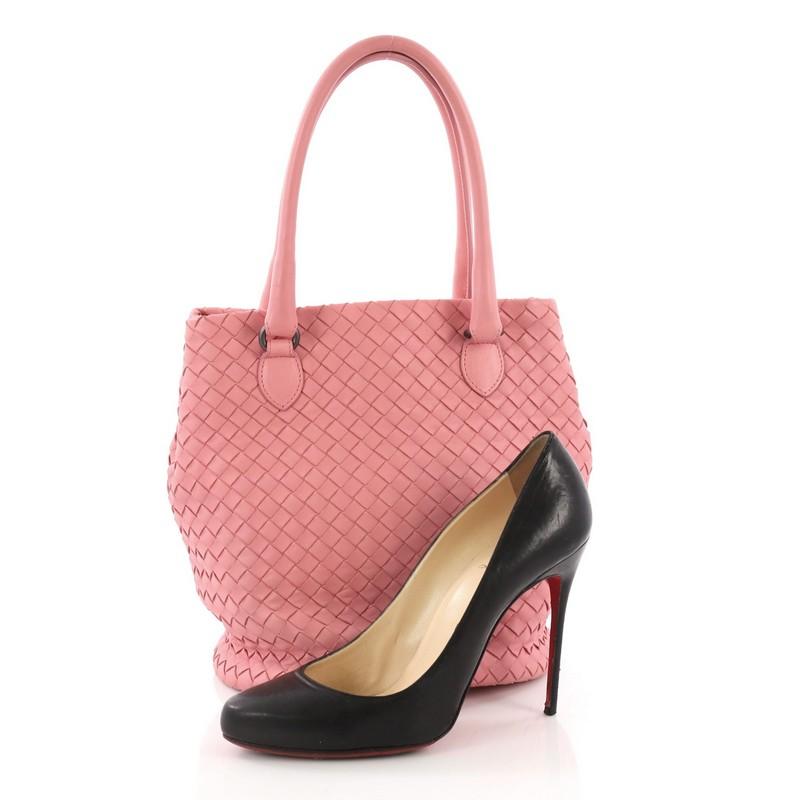 This Bottega Veneta Bucket Bag Intrecciato Nappa Small, crafted in pink intrecciato nappa leather, features dual rolled leather handles, side snap buttons, and gunmetal-tone hardware. It opens to a brown microfiber interior with slip and zip pockets