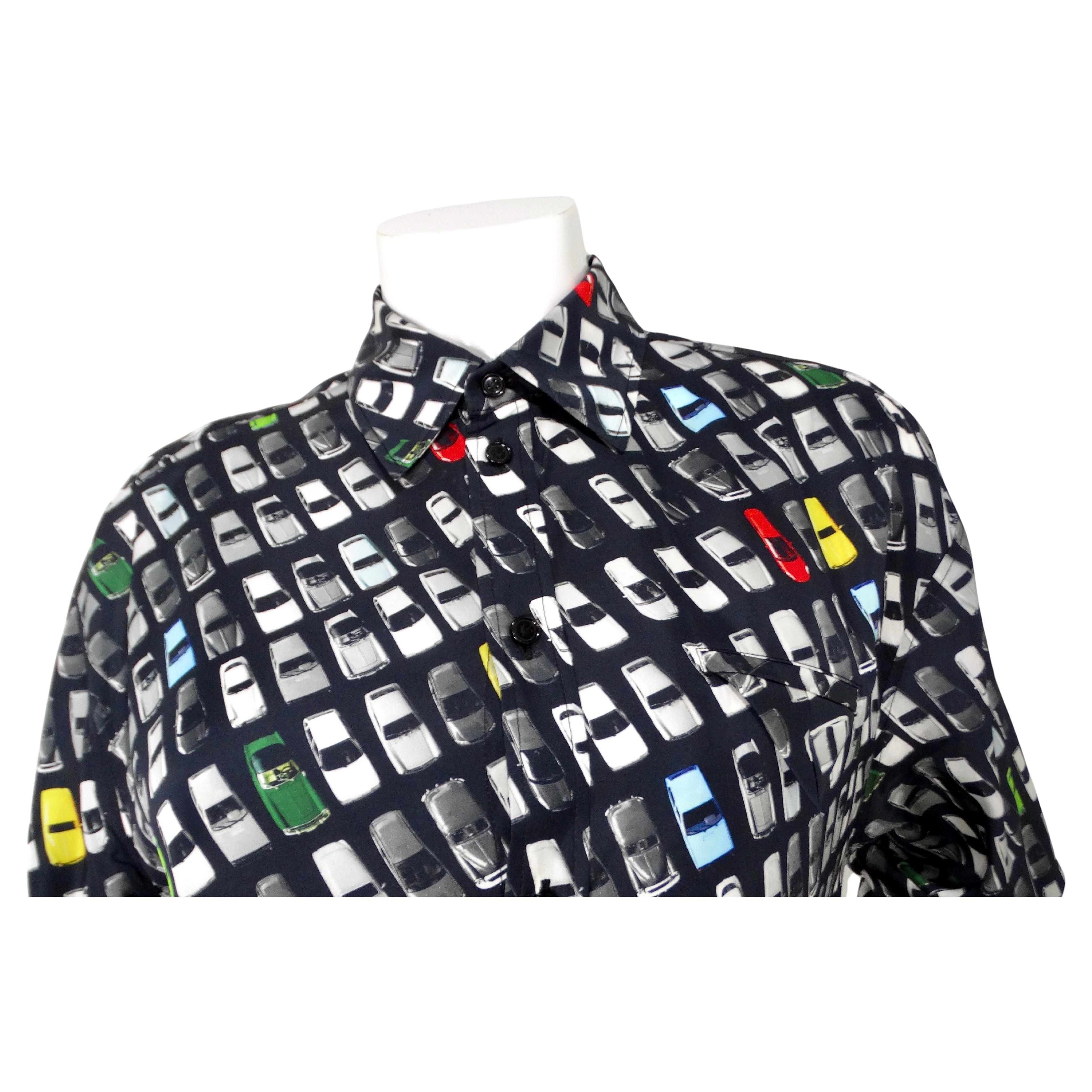Il Bottega Veneta Car Print Button-Up Shirt Dress è un pezzo sorprendente e sofisticato che esemplifica la miscela di lusso e stile contemporaneo tipica del marchio. Questo abito presenta un'accattivante stampa di ispirazione automobilistica che