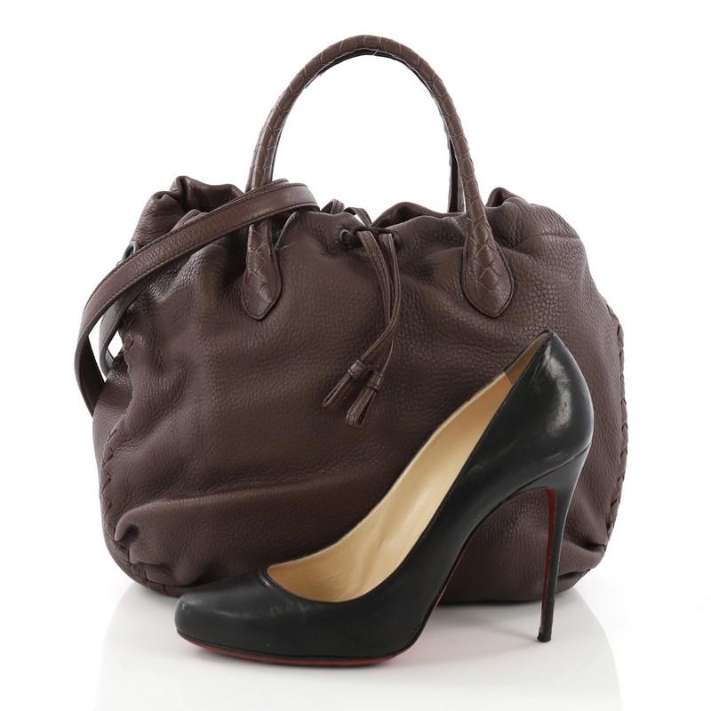 This Bottega Veneta Convertible Drawstring Tote Leather with Intrecciato Detail Medium, crafted in burgundy leather with intrecciato detail, features dual rolled handles and gunmetal-tone hardware. Its two compartment drawstring closures opens to a