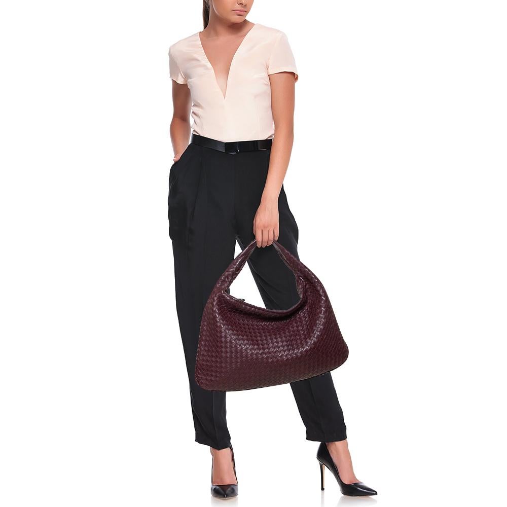 The excellent craftsmanship of this Bottega Veneta handbag ensures a brilliant finish and a rich appeal. Woven from leather in their signature Intrecciato pattern, the burgundy bag is provided with minimal bronze-tone hardware. It features a loop