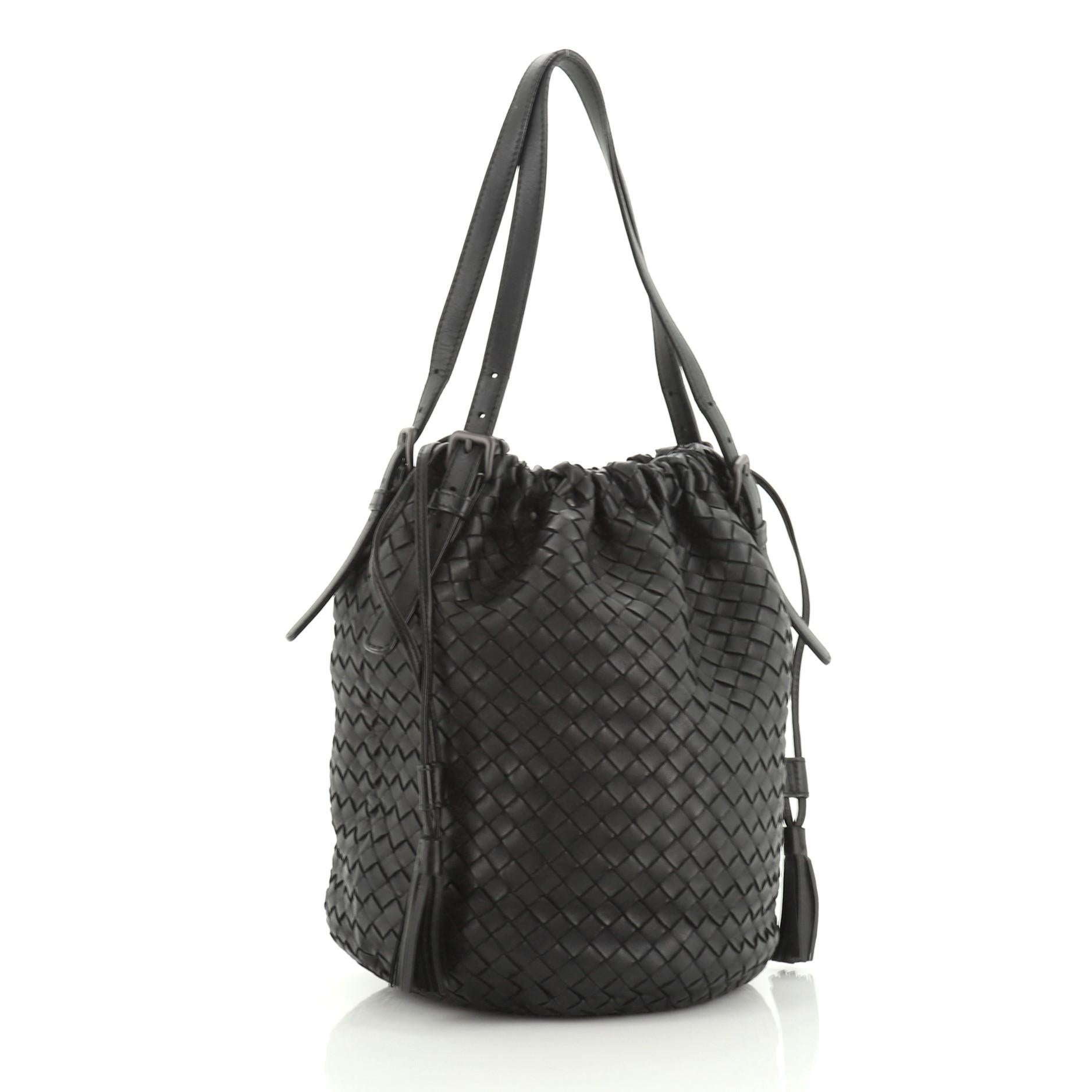 This Bottega Veneta Drawstring Tassel Bucket Bag Intrecciato Nappa Small, crafted from black intrecciato nappa leather, features adjustable leather straps and matte gunmetal-tone hardware. Its drawstring closure opens to a neutral suede interior
