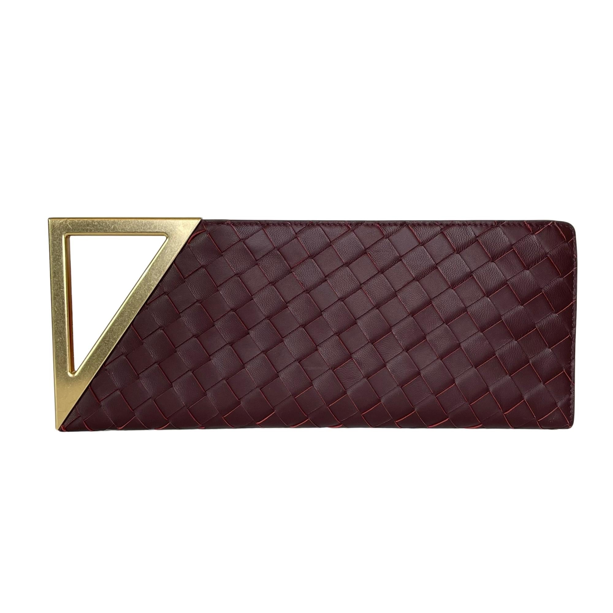 This Bottega clutch is made with intrecciato (woven) leather and features a gold-tone geometric handle, zip closure, logo zipper puller and orange suede interior lining. 

COLOR: Burgundy / Merlot
MATERIAL: Leather
MEASURES: H 5” x L 13” x D