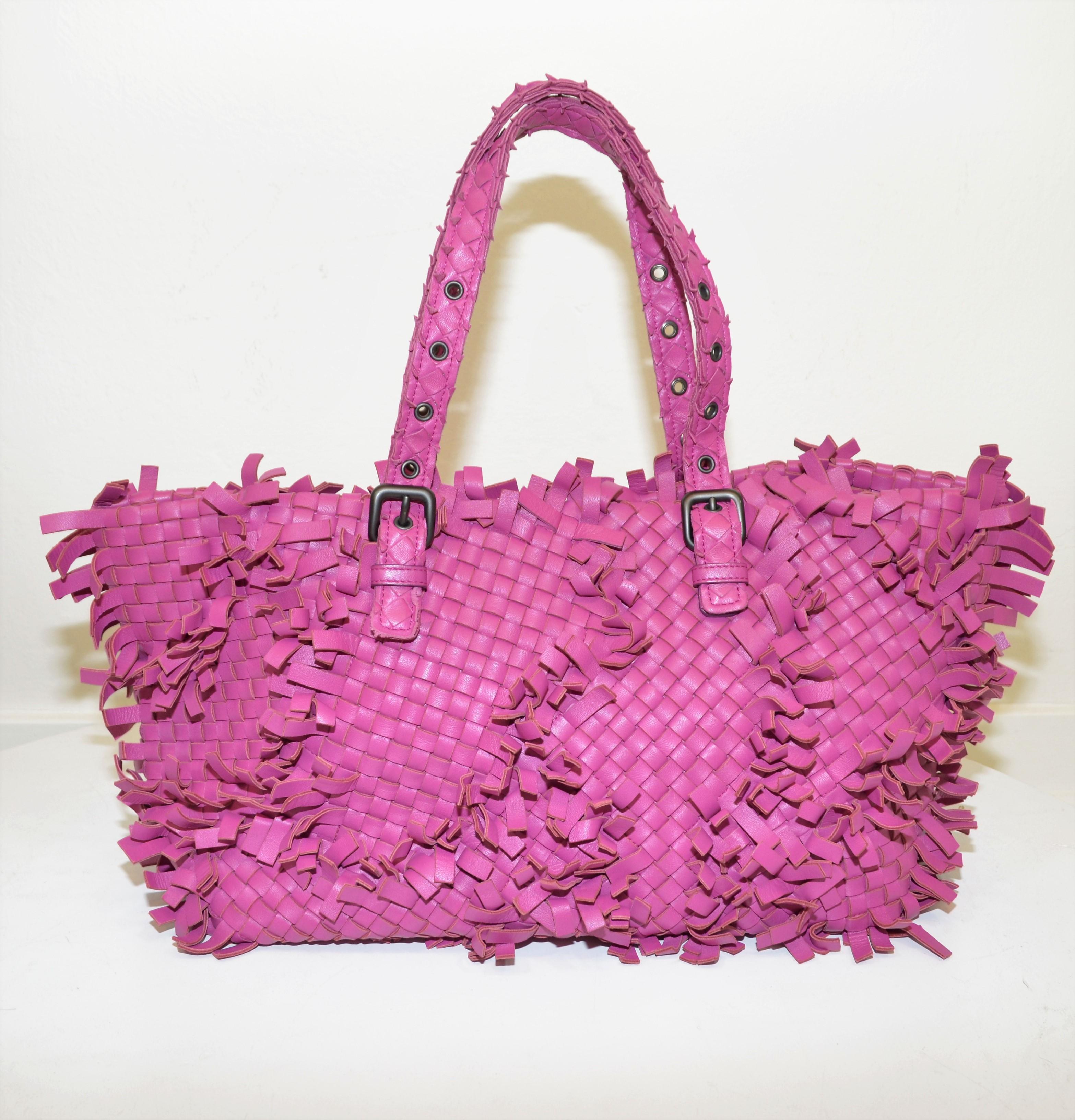 Bottega Veneta tote featured in a raspberry color with fringed leather and an open top. Tote has two adjustable handles attached by gunmetal hardware. Full suede interior lining with one slip pocket and one zippered pocket. Hand mirror is included.