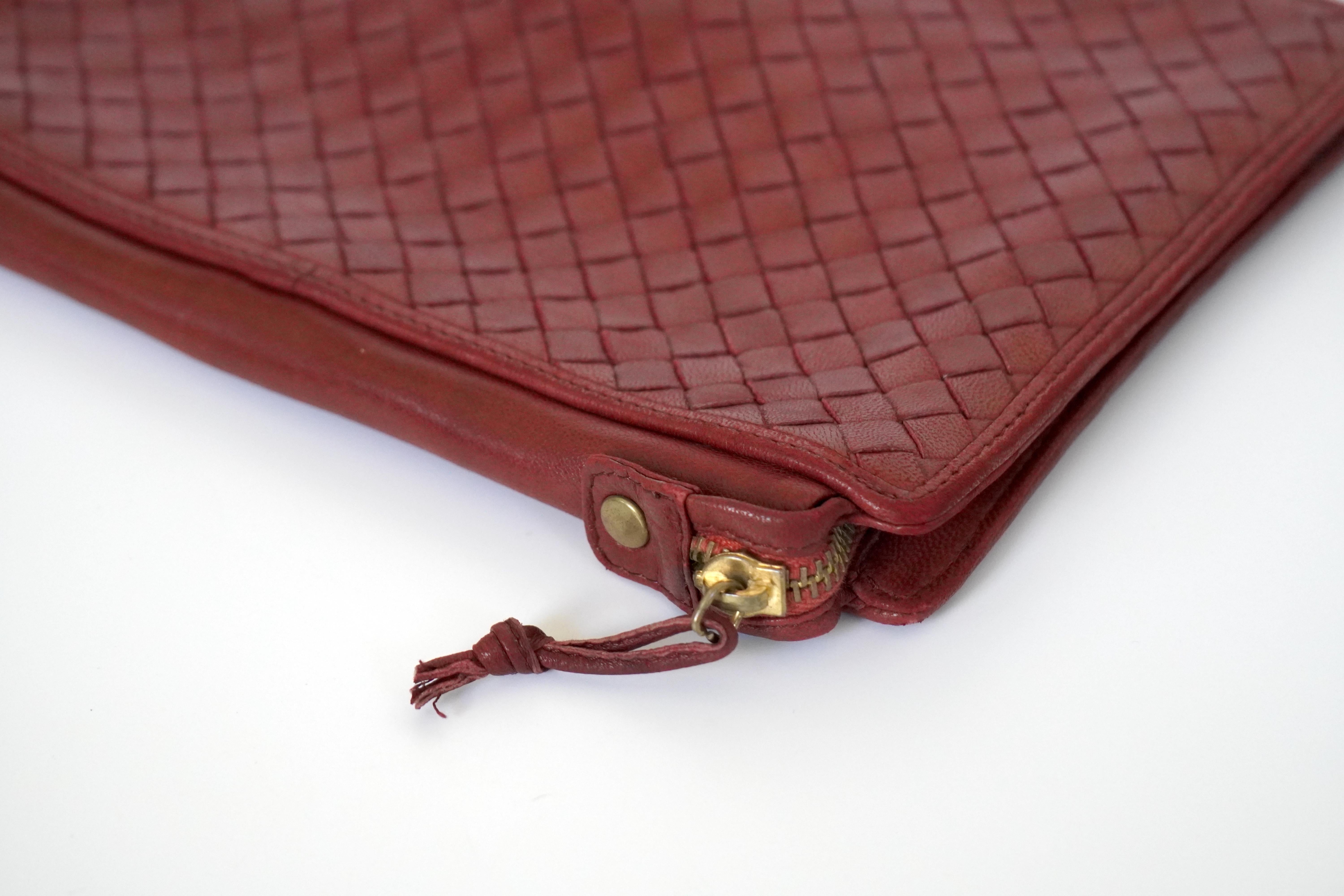 This Bottega Veneta clutch bag, crafted in the iconic Intrecciato weave, exudes sophistication in a subtle dark rosa red hue. Measuring 10 inches by 7 inches, it strikes a balance between style and practicality. The interior reveals a well-designed
