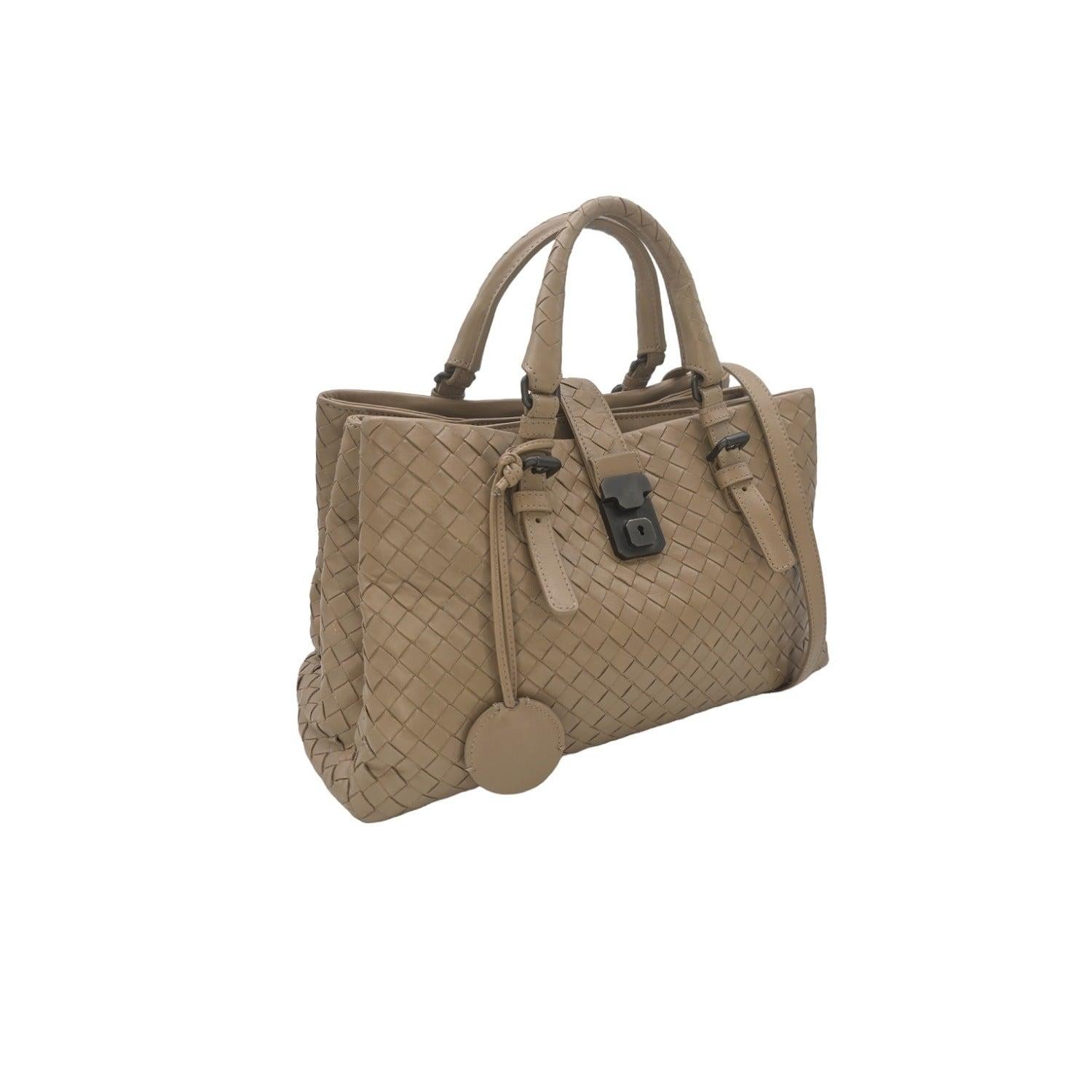 Introducing the Bottega Veneta Intrecciato Roma Small Top Handle Bag, designed by expert craftsmen in Italy. Made with the signature Intrecciato leather, this bag features convenient dual rolled top handles and a removable strap for versatile wear.