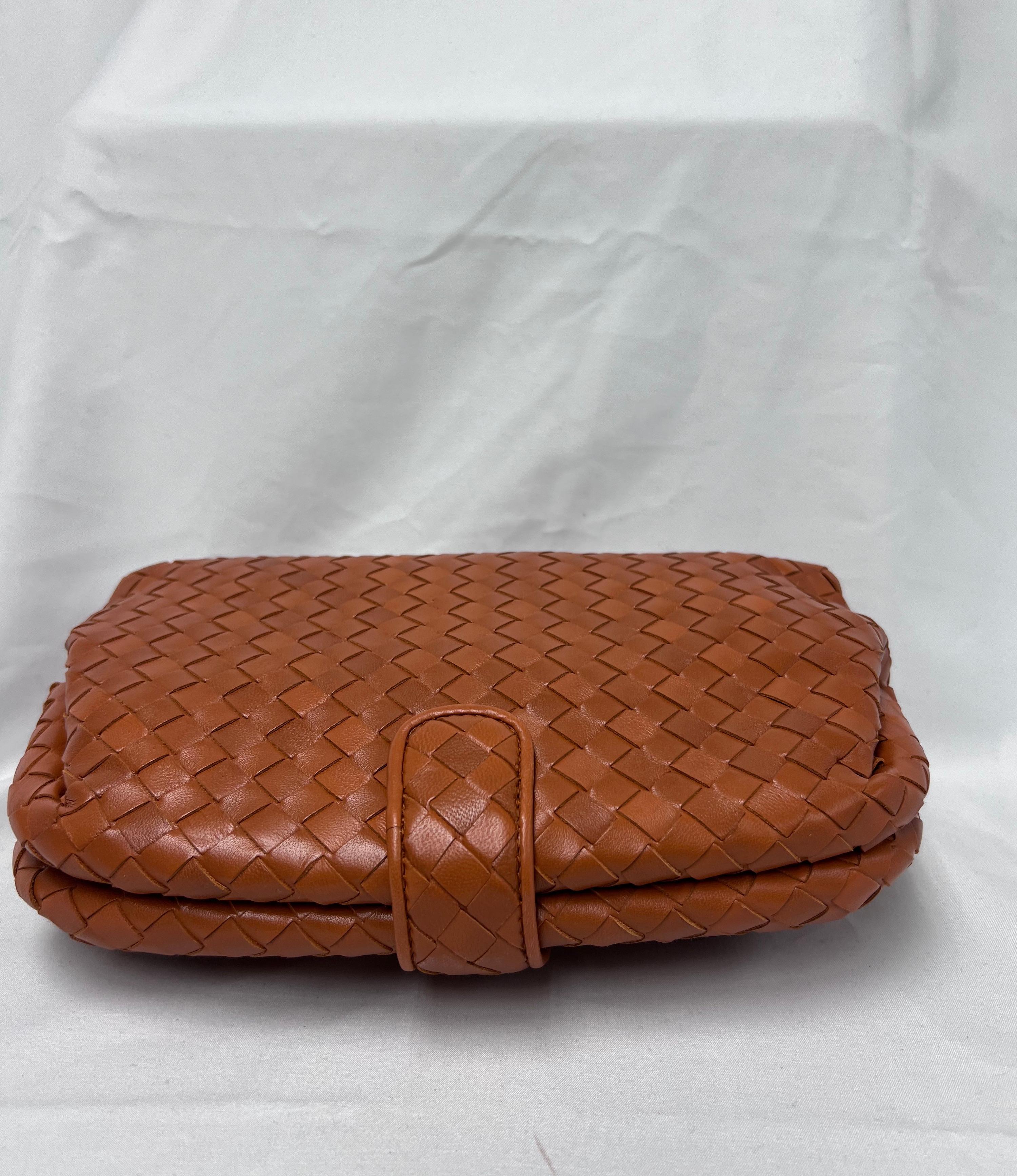 The Lauren 1980 clutch is a timeless accessory made from sumptuous orange camel intrecciato leather, adorned with dark silver brass detailing. It features a classic snap closure, a taupe beige suede lining, and a practical zipped pocket that